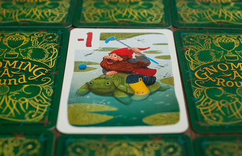 Gnoming A Round - Playing card with colorful illustration of a red-cloaked gnome riding a green turtle, surrounded by green backs with gold.