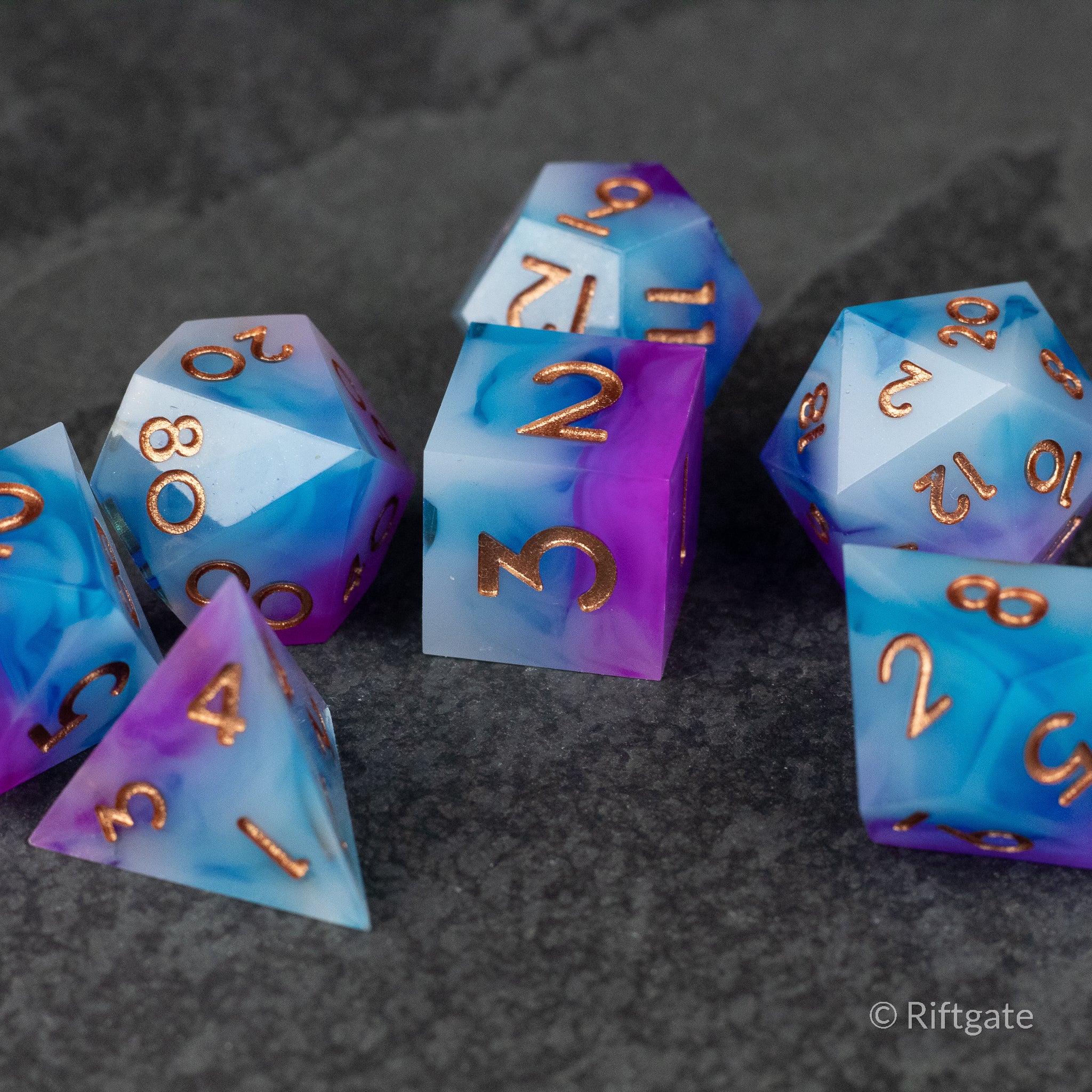 Arcane Tempest Dice Set - Seven polyhedral dice with sharp edges in blue and purple swirls, featuring gold numbers.