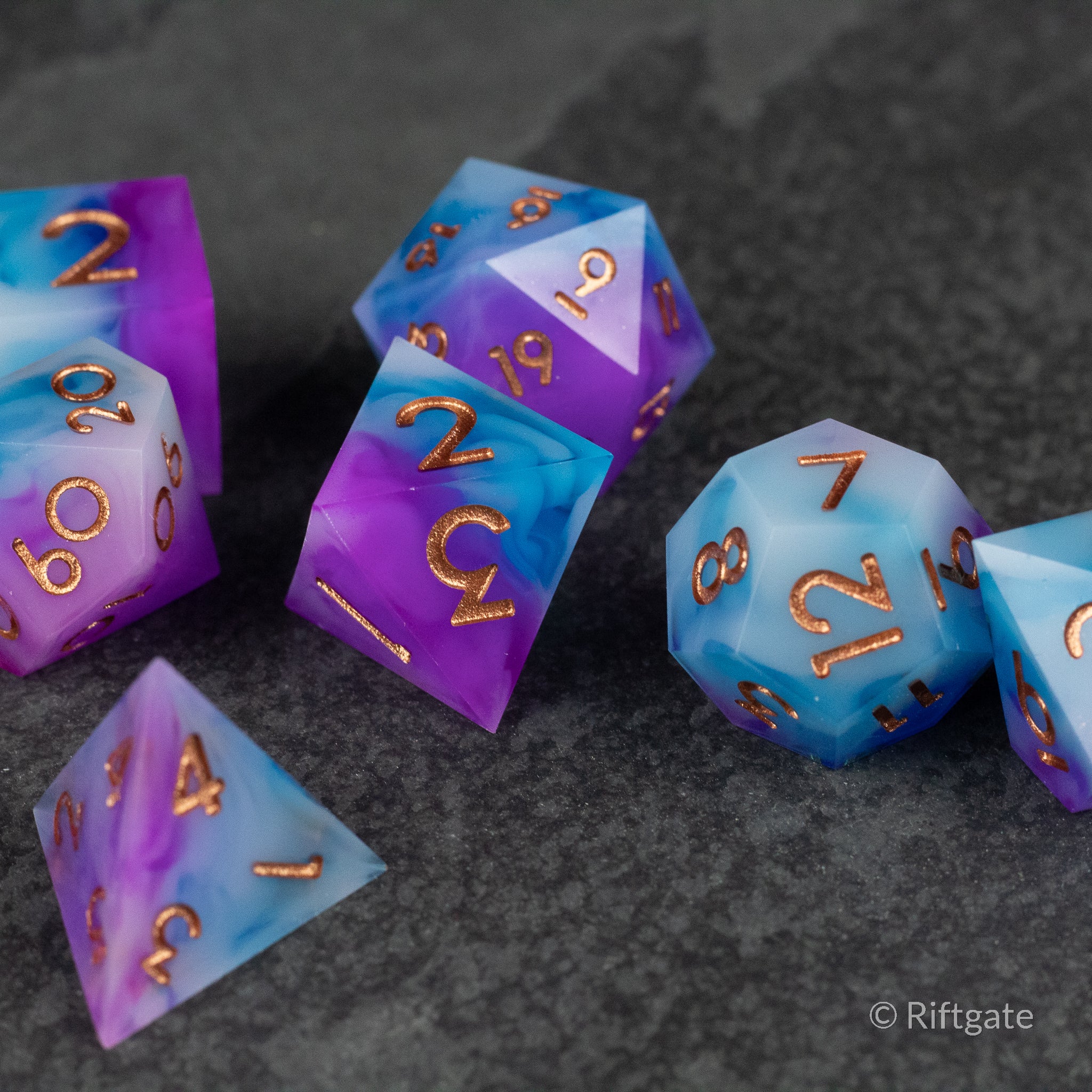 Arcane Tempest Dice Set - Purple and blue sharp-edged polyhedral dice set with gold numbering on a dark surface.