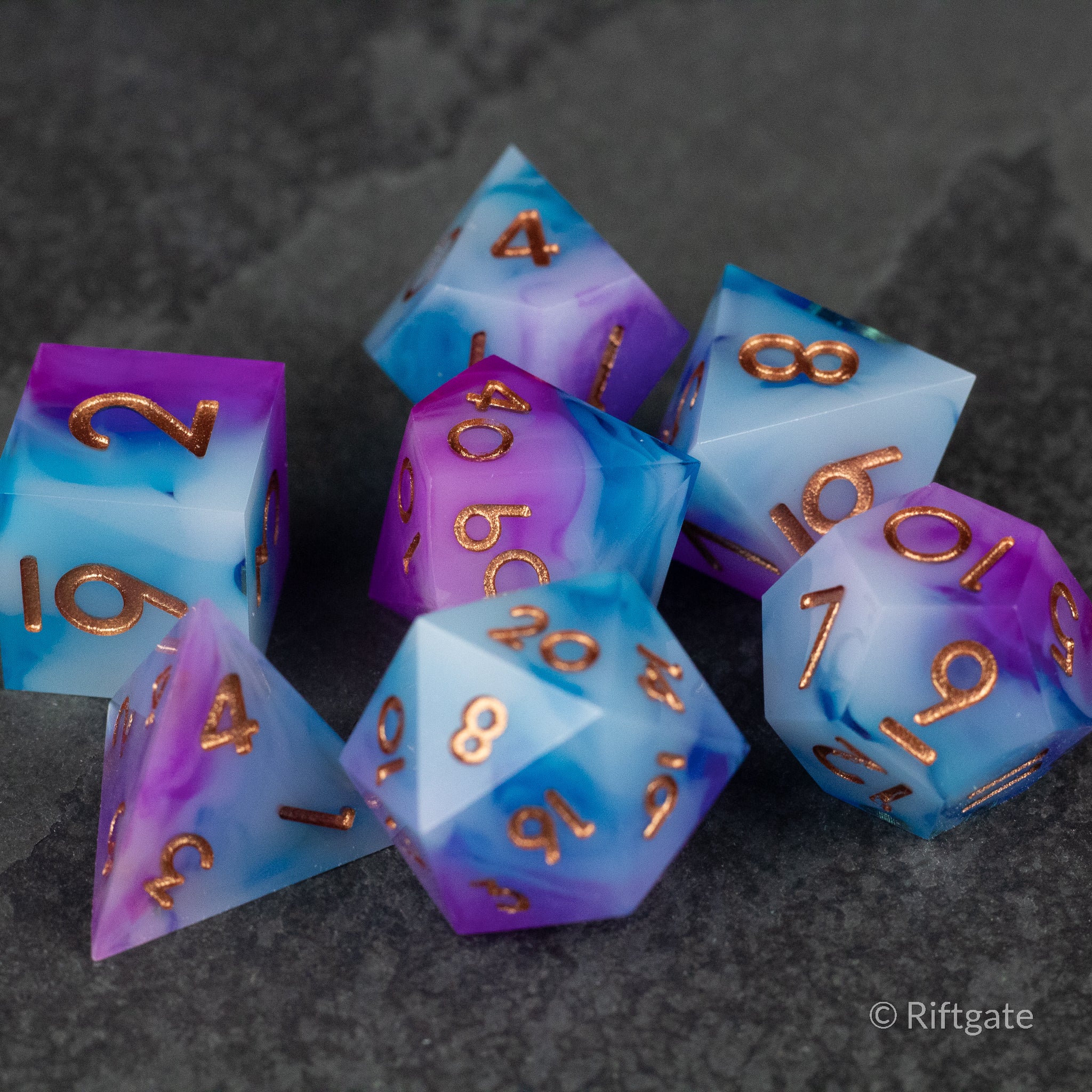 Arcane Tempest Dice Set - Set of seven sharp-edged polyhedral dice with swirling blue and purple colors and gold numbering.
