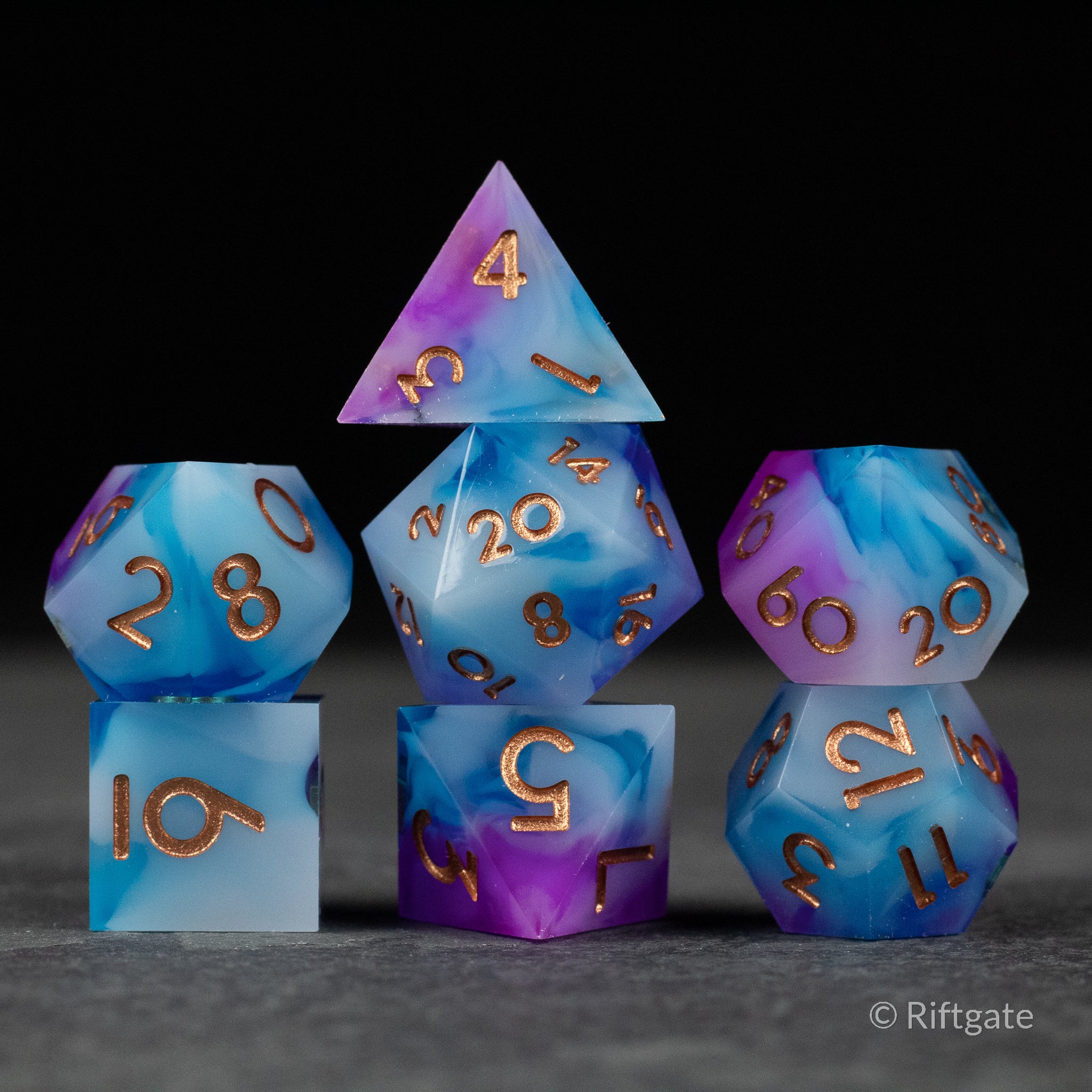 Arcane Tempest Dice Set - Set of seven sharp-edged dice with a swirling gradient of blue and purple, featuring gold numbering and angular shapes for.