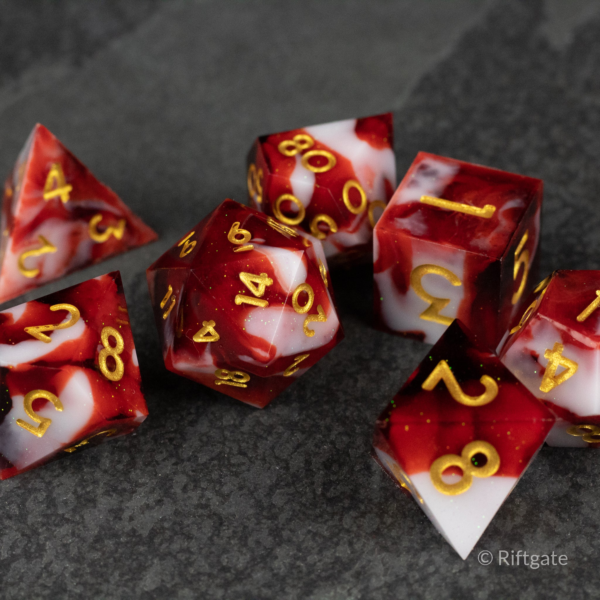 Blood and Snow Dice Set - Seven red and white sharp-edged polyhedral dice with gold numbers on a dark surface.