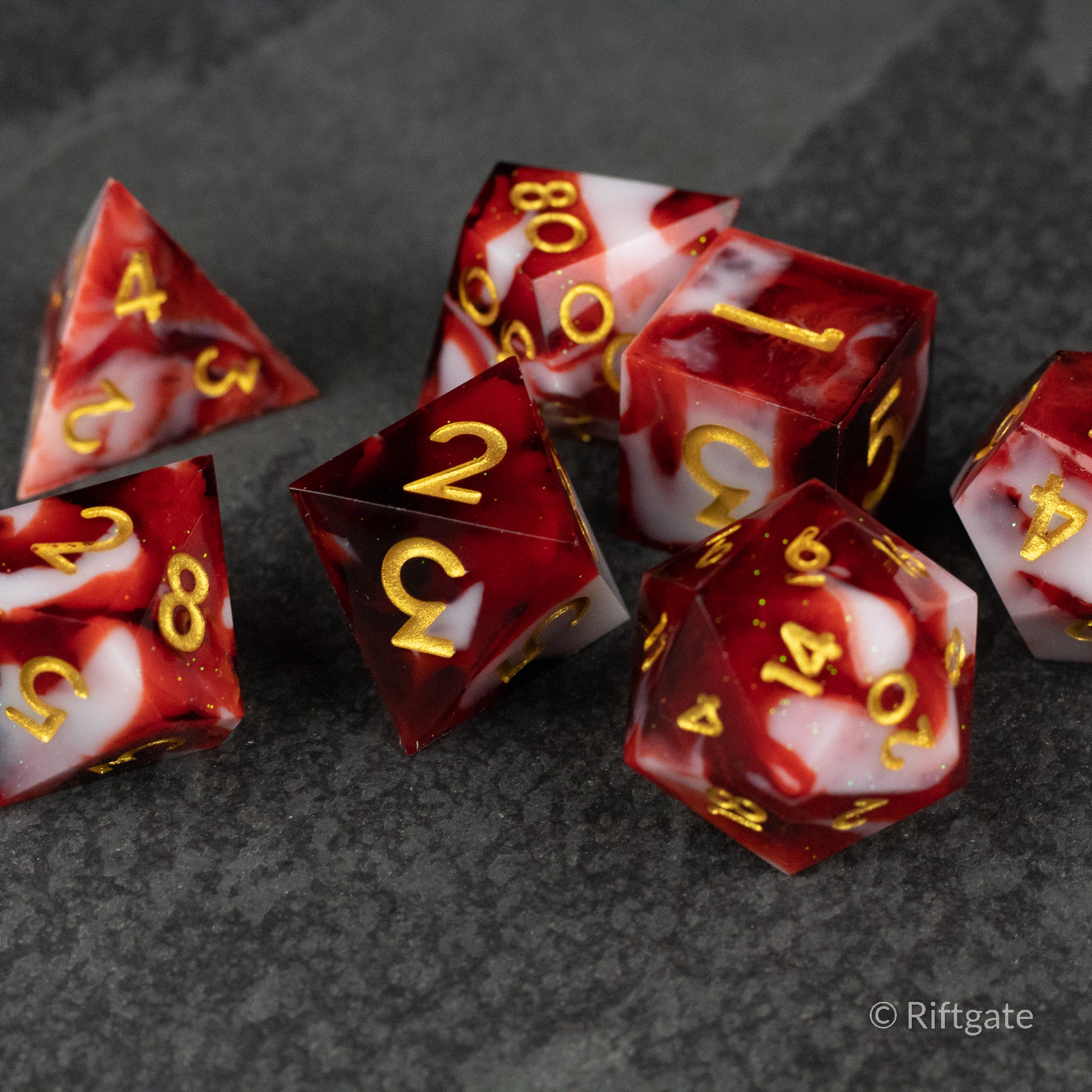 Blood and Snow Dice Set - Sharp-edged red and white marbled dice with gold numbering on a dark gray surface.