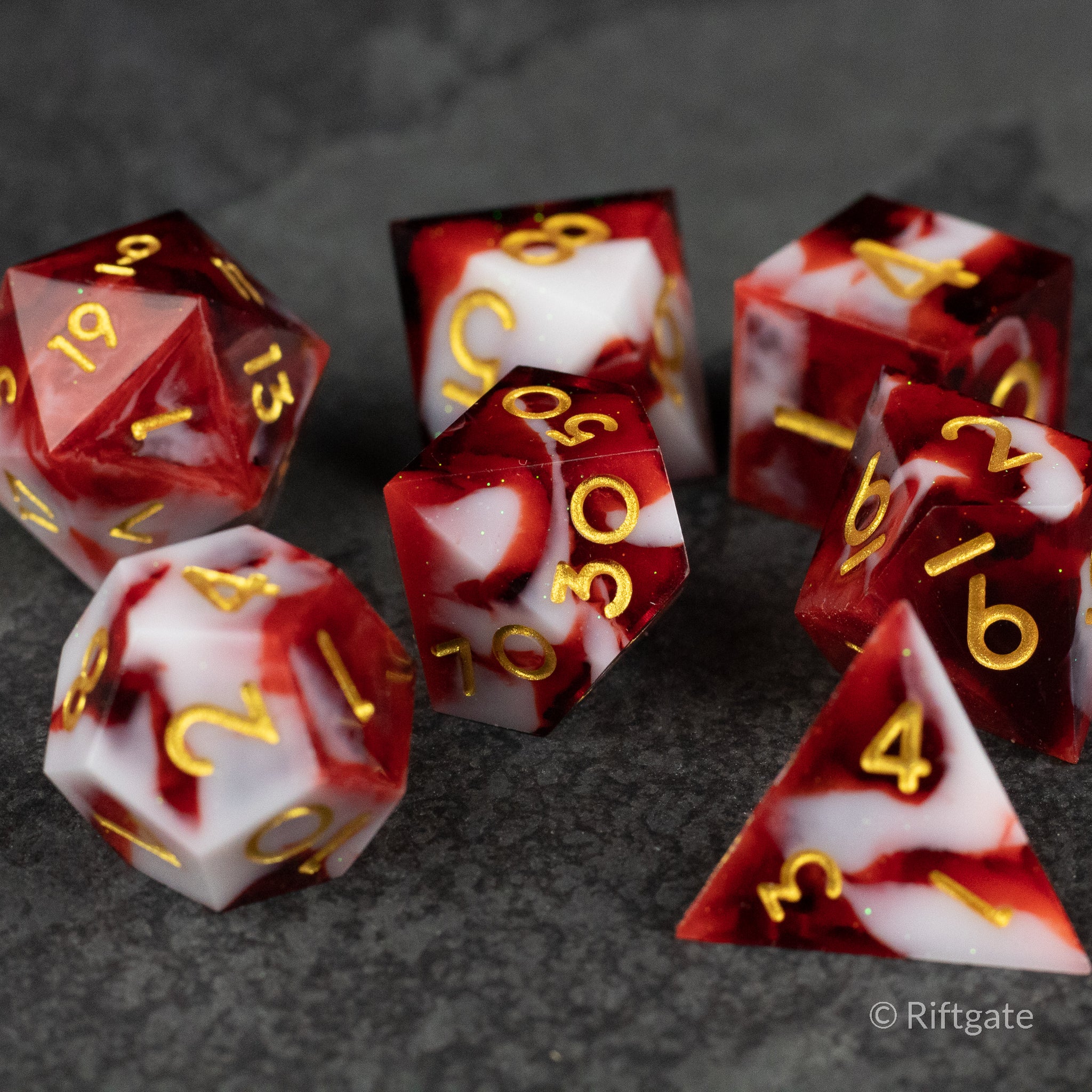 Blood and Snow Dice Set - Set of seven sharp-edged polyhedral dice with red and white marbled faces and gold numbers.