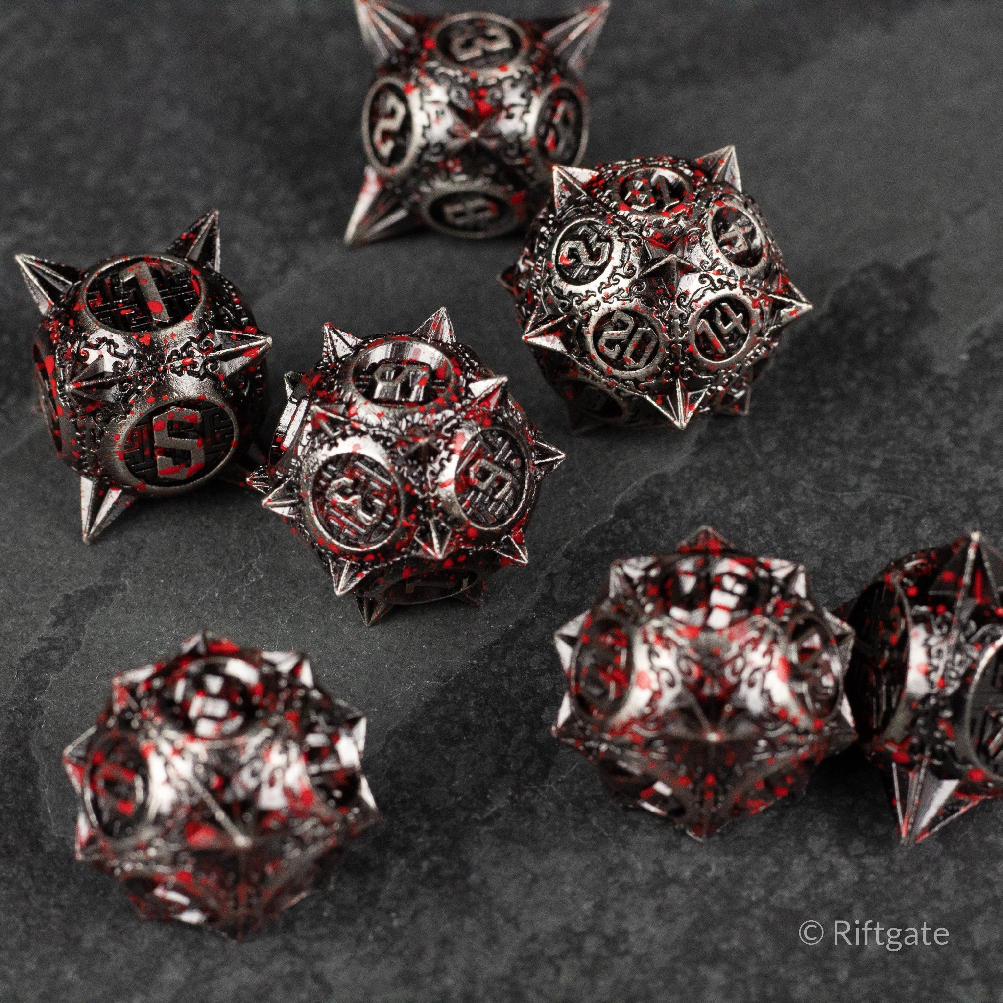 Bloody Morning Star Metal Dice Set - Set of seven black metal spiked dice with red blood splatter and white numbering on a dark textured surface.