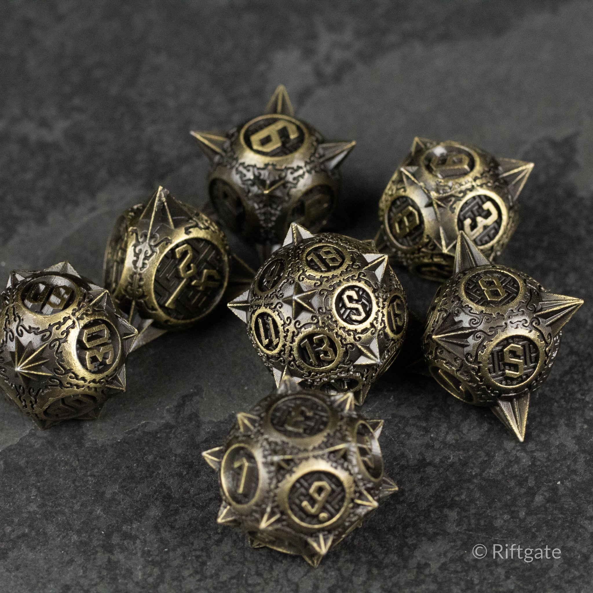Bronze Morning Star Metal Dice Set - Bronze metal dice set with spiked morning star design and black engraved numbers on dark stone surface.