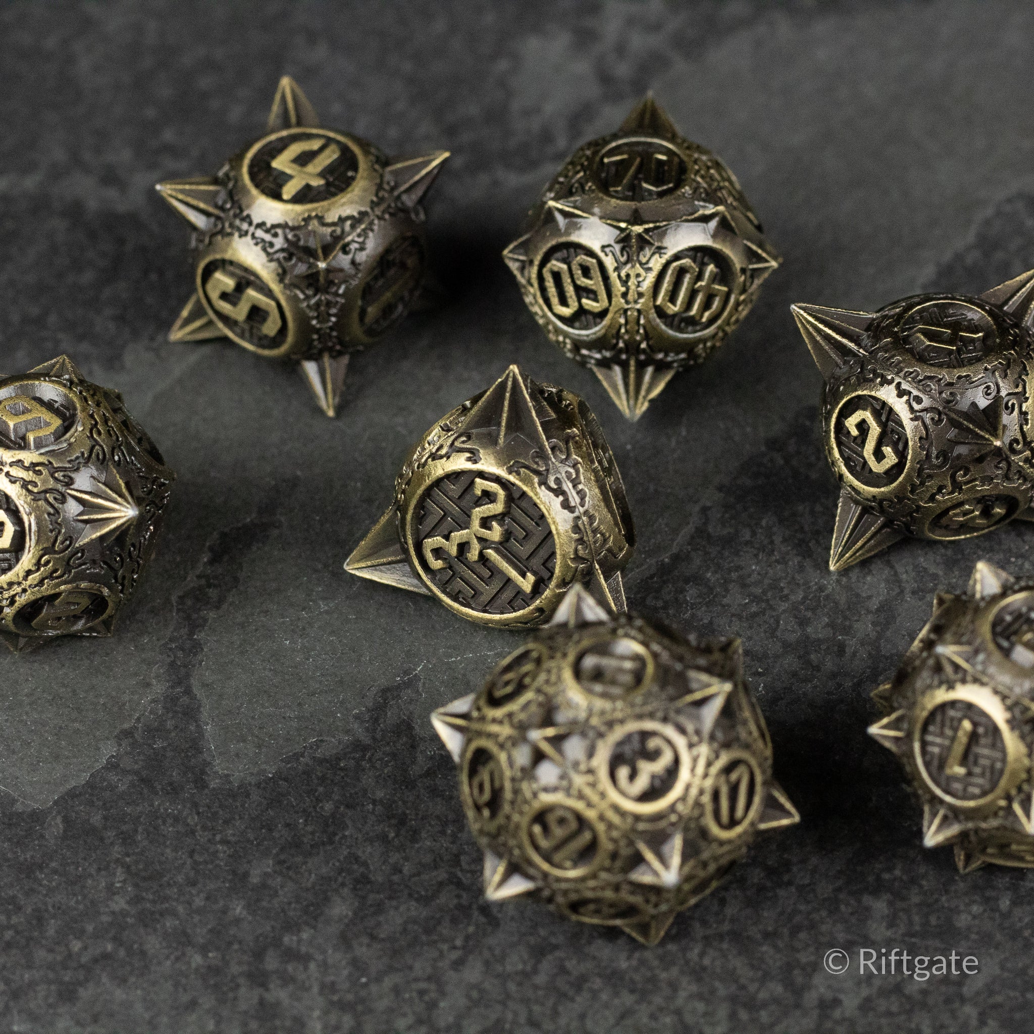 Bronze Morning Star Metal Dice Set - Bronze metal polyhedral dice with spiked edges and engraved numbers on a dark stone surface.