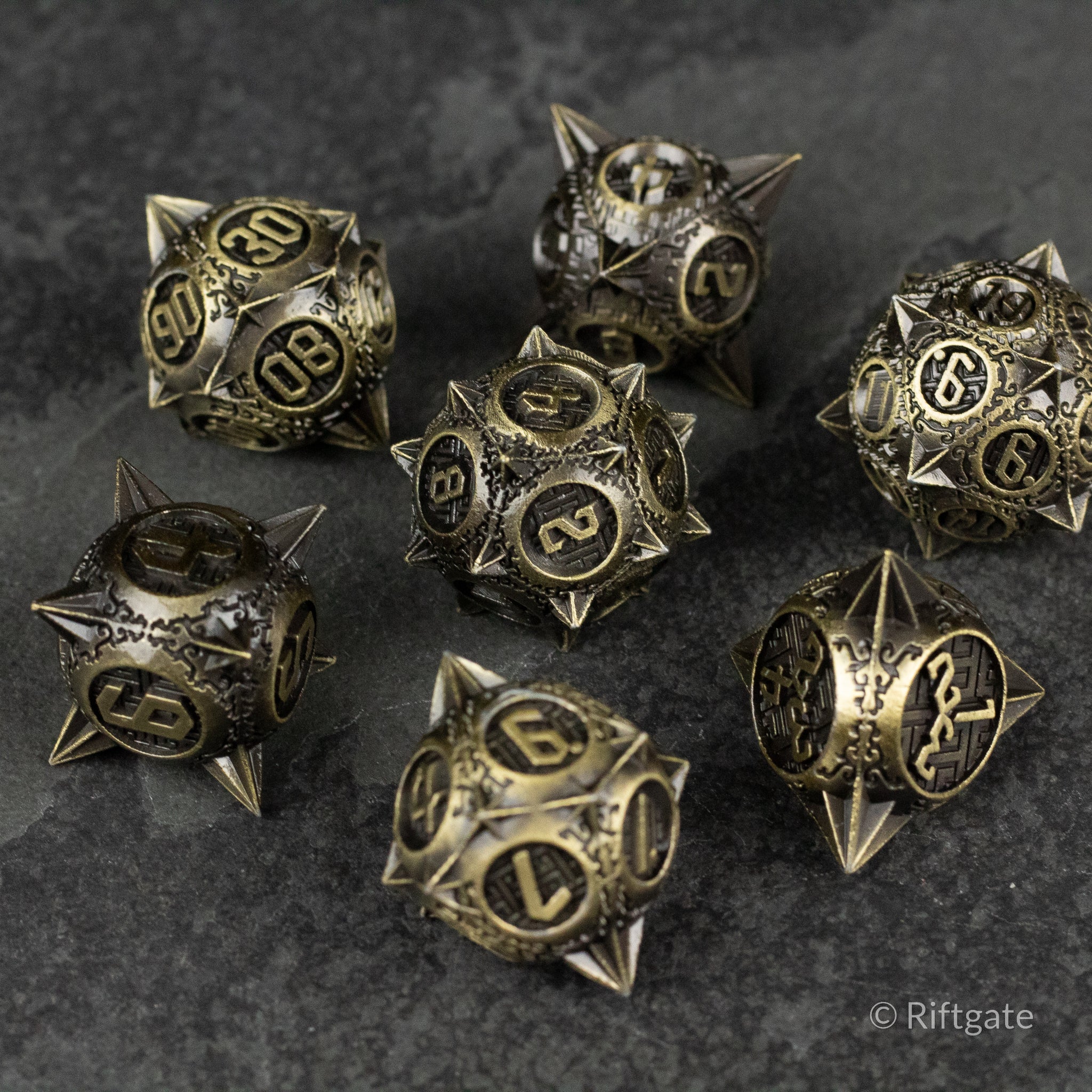 Bronze Morning Star Metal Dice Set - Bronze metal dice set with spiked morning star design and engraved numbers on dark stone surface.