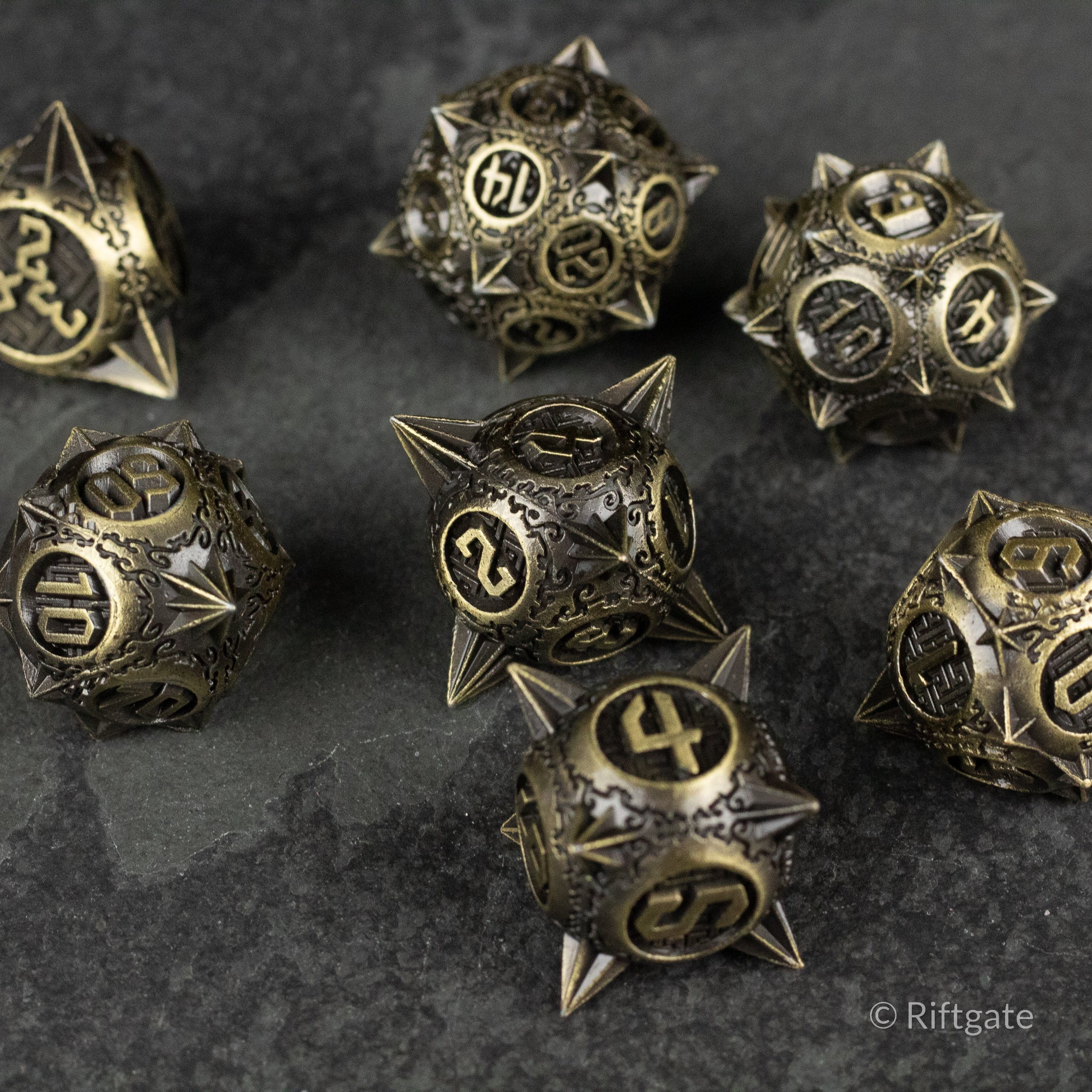 Bronze Morning Star Metal Dice Set - Bronze spiked metal dice set with intricate engravings and black numbering on dark stone surface.