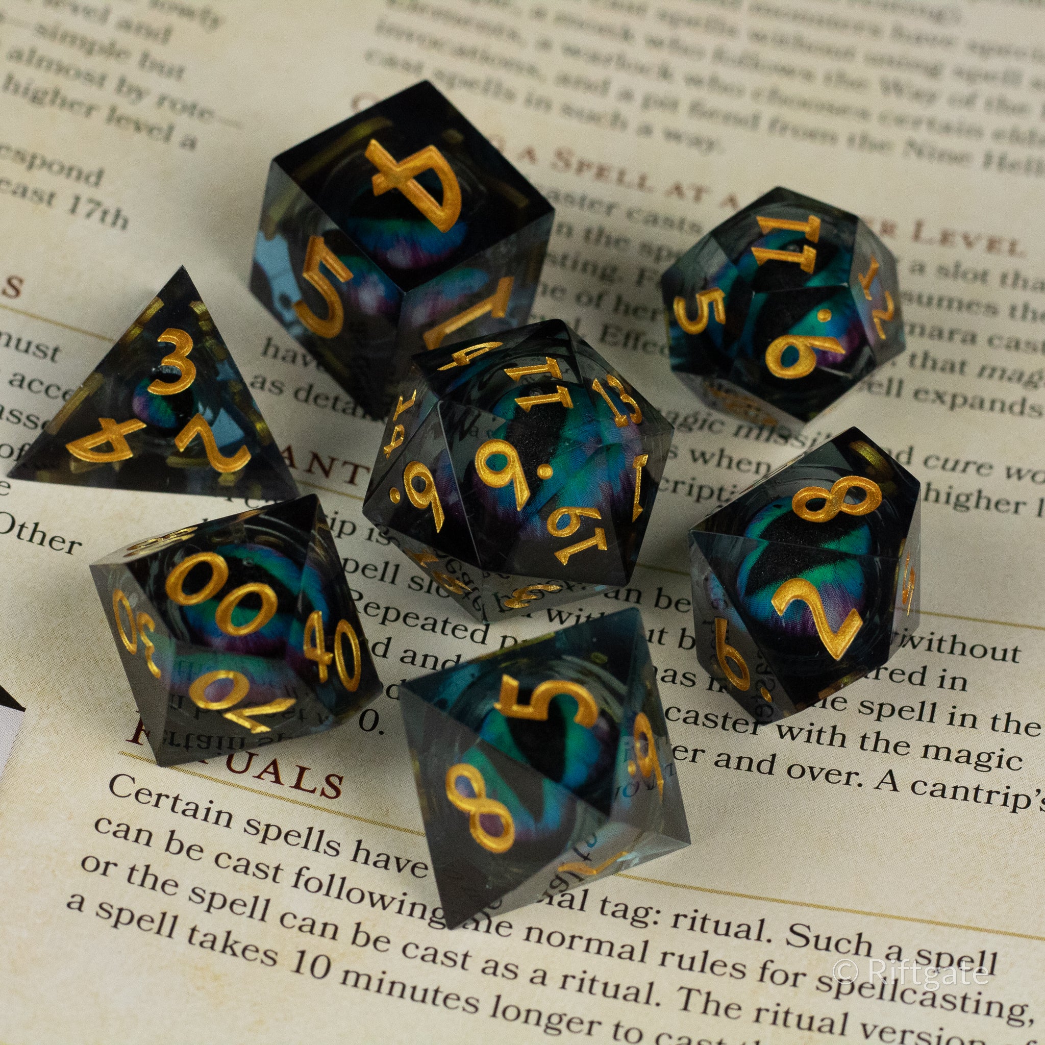 Cosmic Beholder's Eye Dice Set - Seven dark translucent polyhedral dice with swirling blue and black liquid core and sharp golden numbers, designed for.