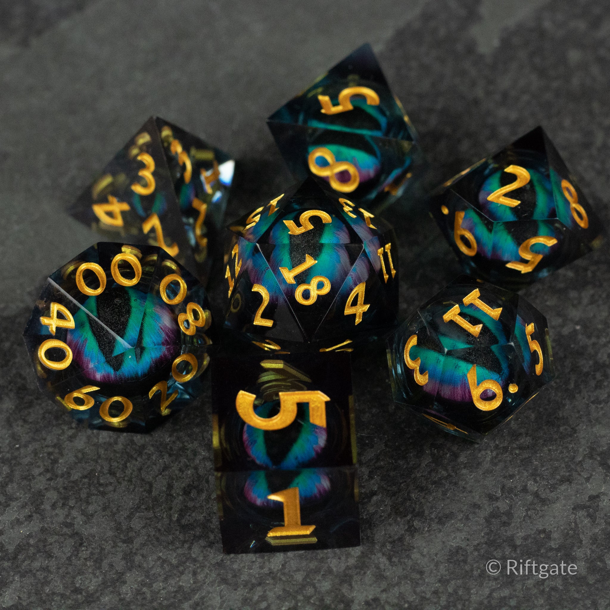 Cosmic Beholder's Eye Dice Set - Black and teal sharp-edged dice set with gold numbers featuring a swirling liquid core design.