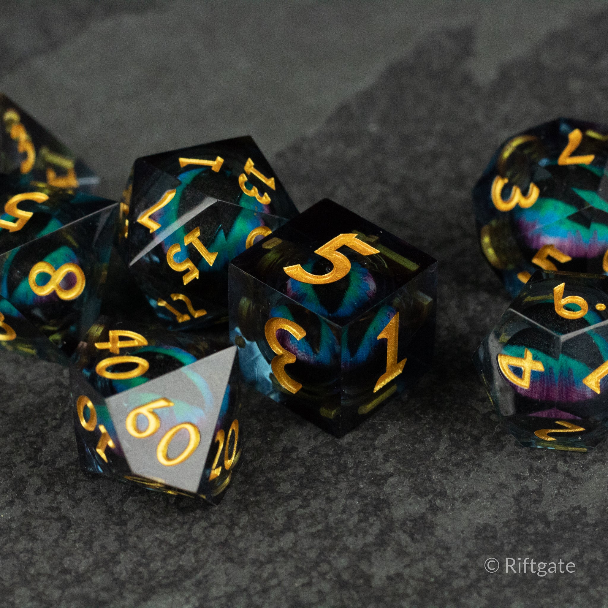 Cosmic Beholder's Eye Dice Set - Sharp-edged polyhedral dice set with black and vibrant blue-green liquid core and gold numbers.