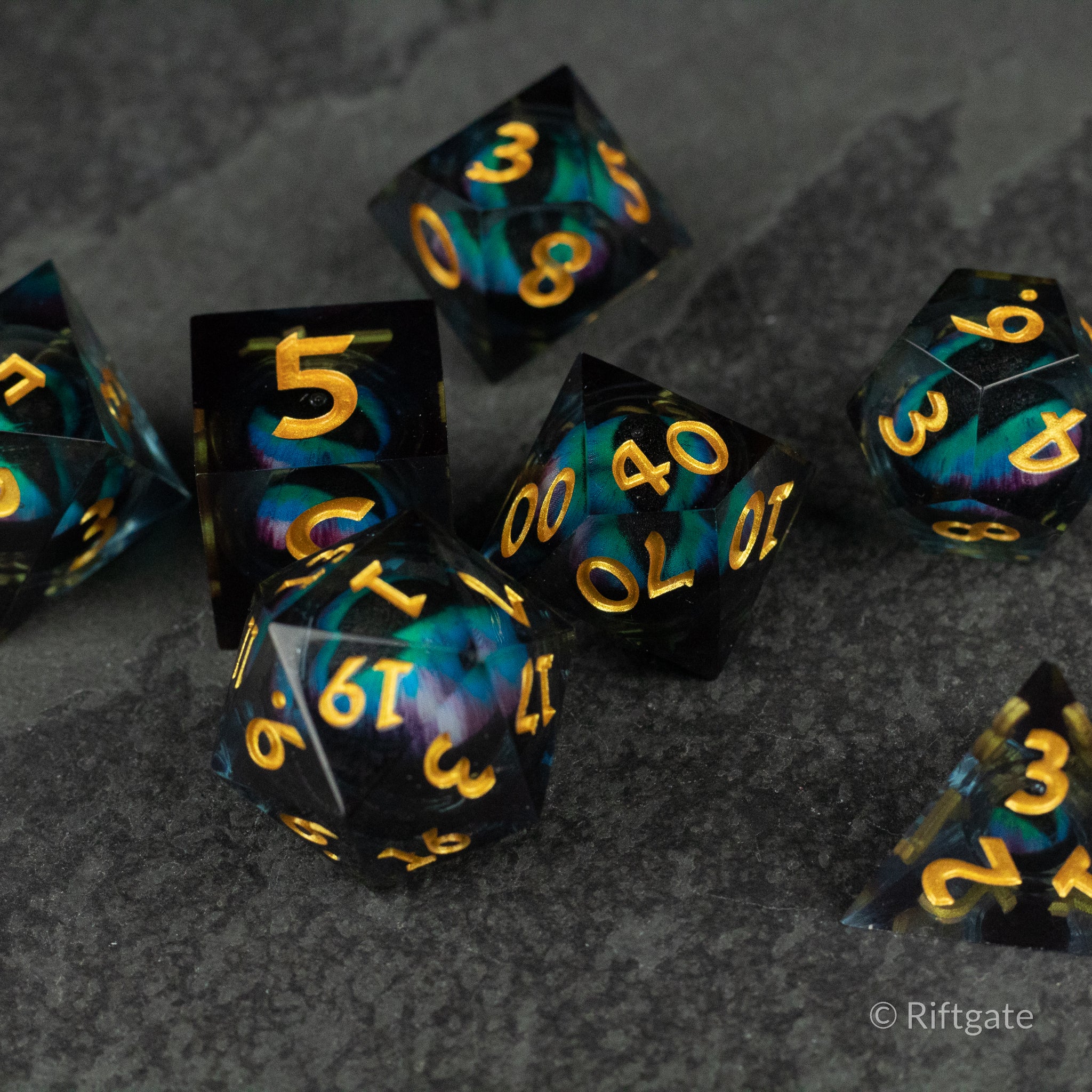 Cosmic Beholder's Eye Dice Set - Black and teal swirled seven-piece polyhedral dice set with gold sharp-edged numbers.