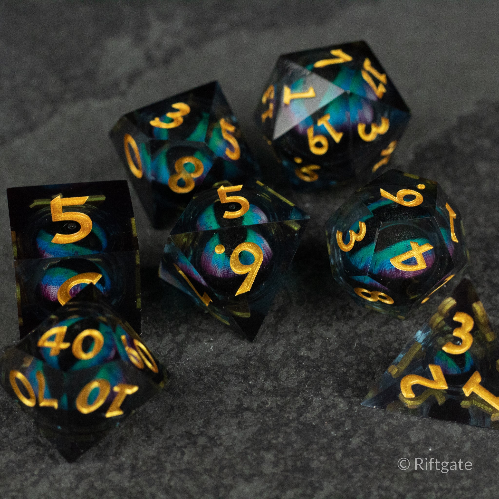 Cosmic Beholder's Eye Dice Set - Set of seven black polyhedral dice with sharp edges, liquid core swirls in blue and purple, gold numbers.