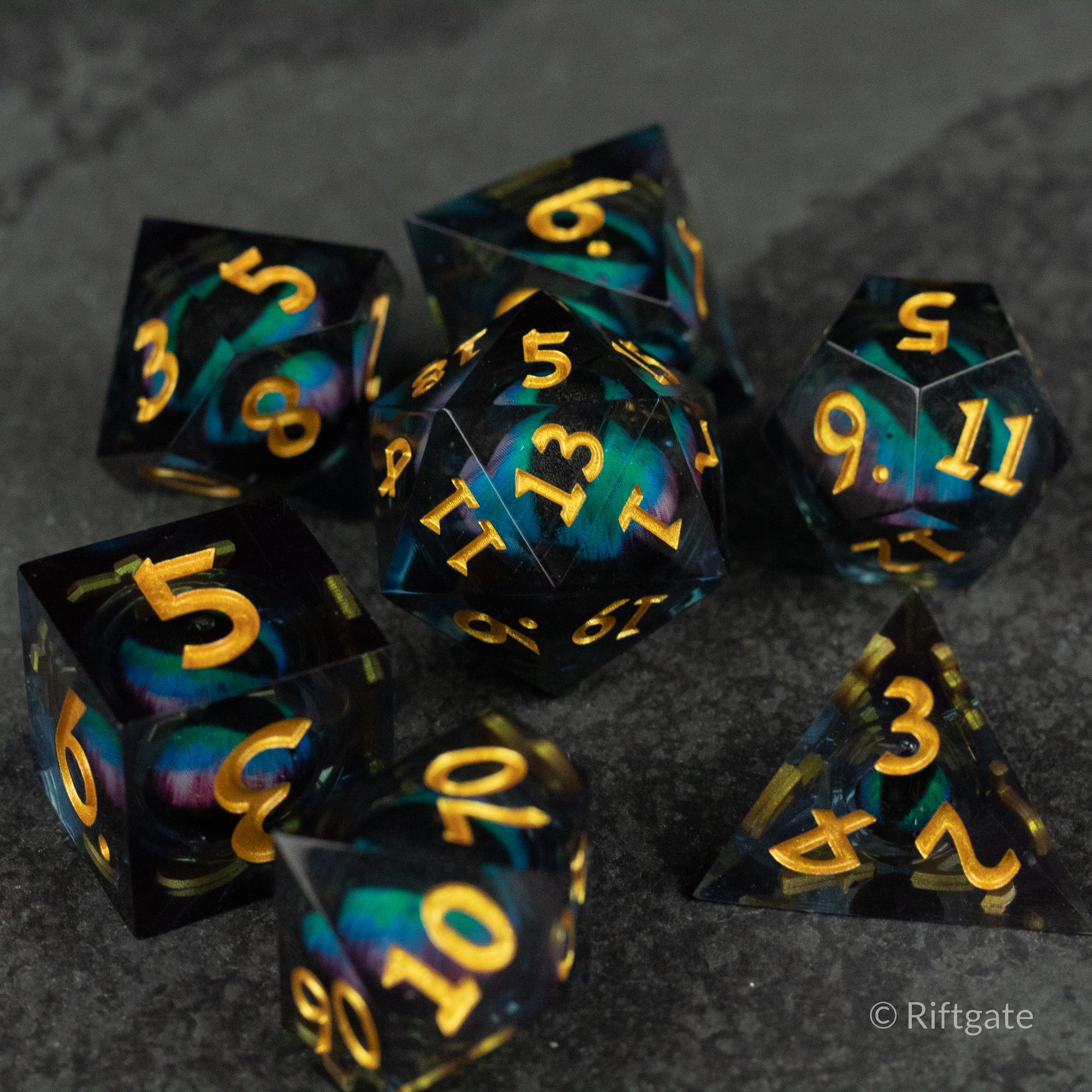 Cosmic Beholder's Eye Dice Set - Set of seven black polyhedral dice with sharp edges, featuring swirling blue and purple liquid cores and gold numbering.