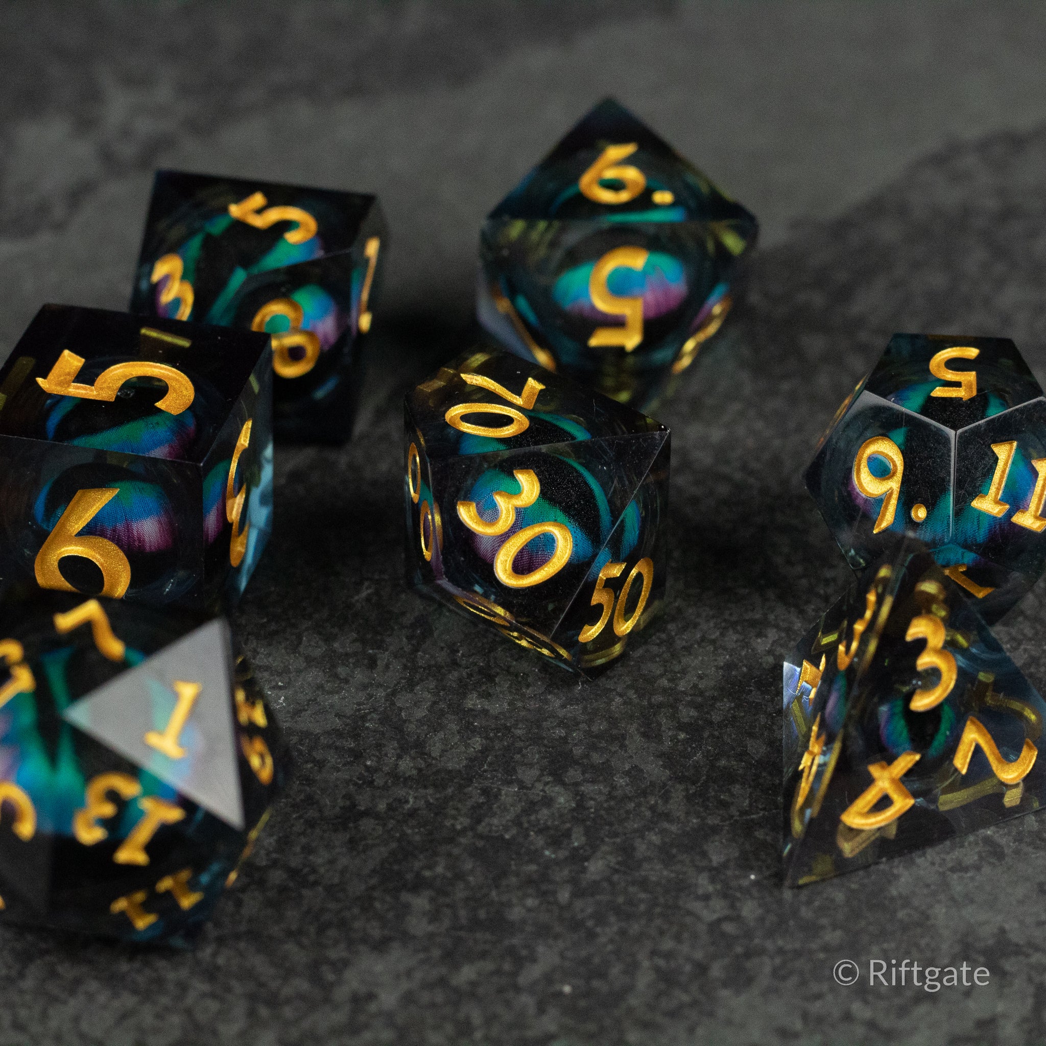 Cosmic Beholder's Eye Dice Set - Set of seven black and teal marbled polyhedral dice with sharp edges and bright gold numbering.