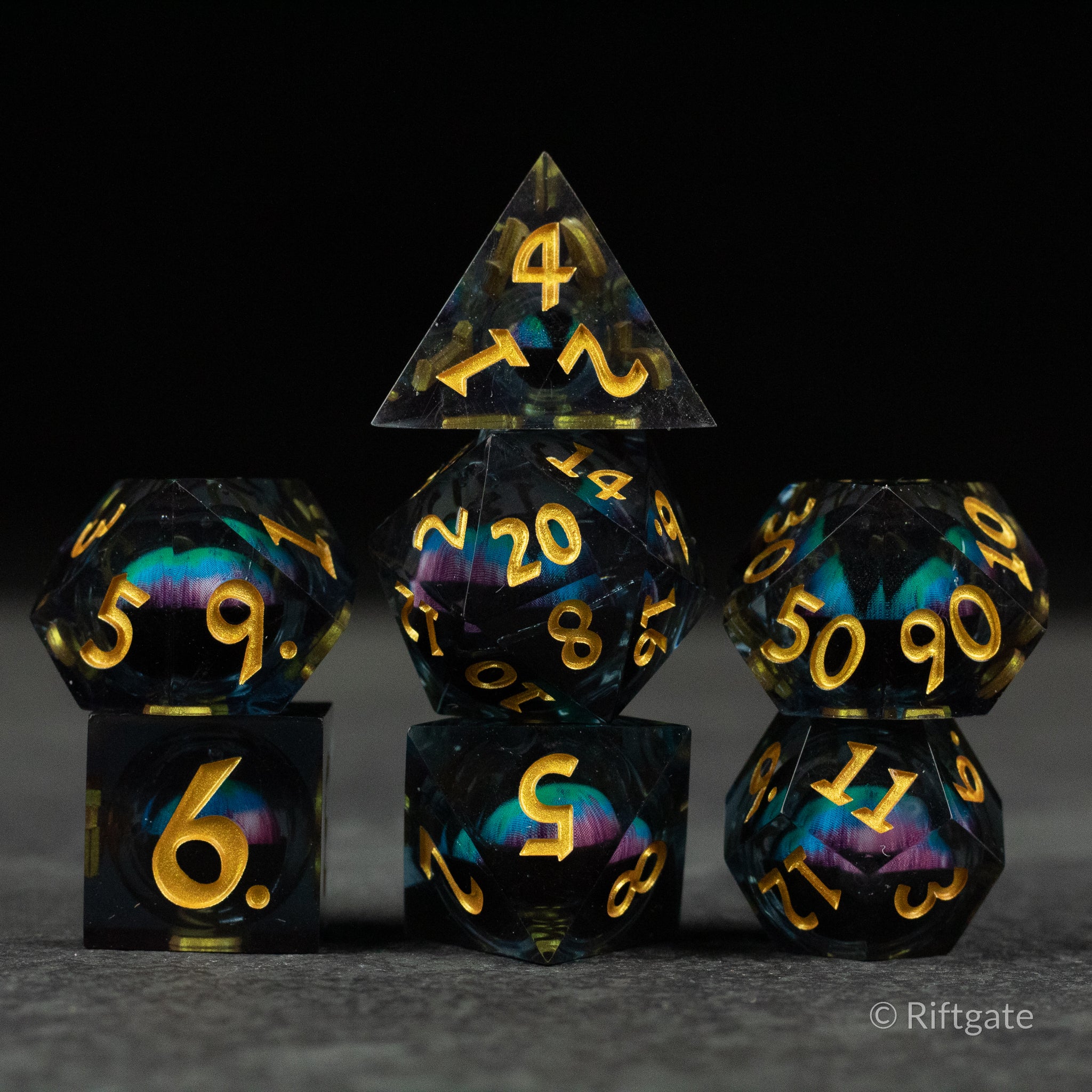 Cosmic Beholder's Eye Dice Set - Sharp-edged black polyhedral dice set with swirling blue, purple, and gold liquid core and gold numbers.