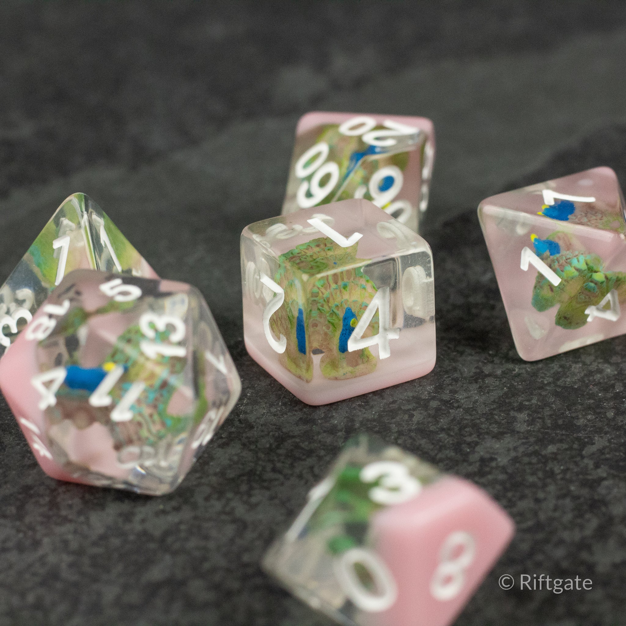 Peacock Dice Set - Set of translucent pink polyhedral dice with green and blue peacock feather inclusions and white numbers.