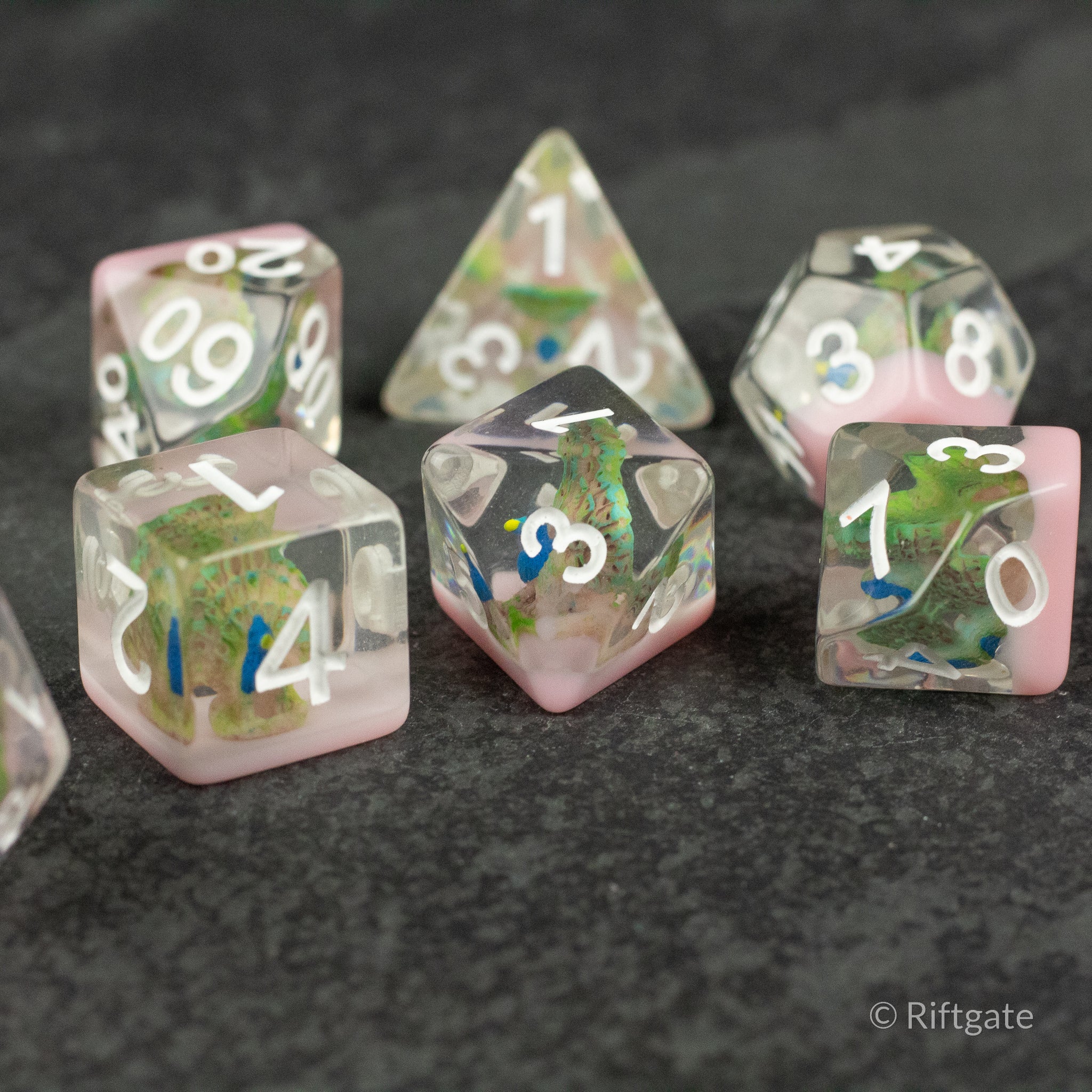 Peacock Dice Set - Translucent polyhedral dice set with pink and green swirls and white numbering on black surface.
