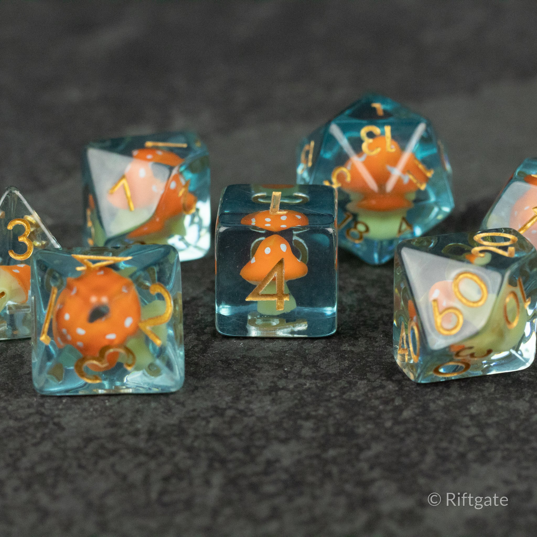 Orange + Blue Resin Mushroom Dice Set - Clear resin dice with embedded orange and blue mushroom shapes and gold numbers on dark surface.