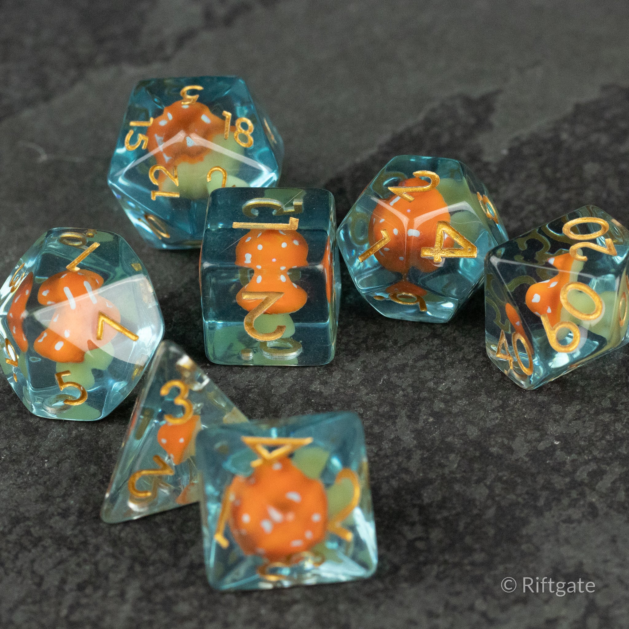 Orange + Blue Resin Mushroom Dice Set - Set of seven translucent blue resin dice with orange mushroom-shaped inclusions and gold numbers.