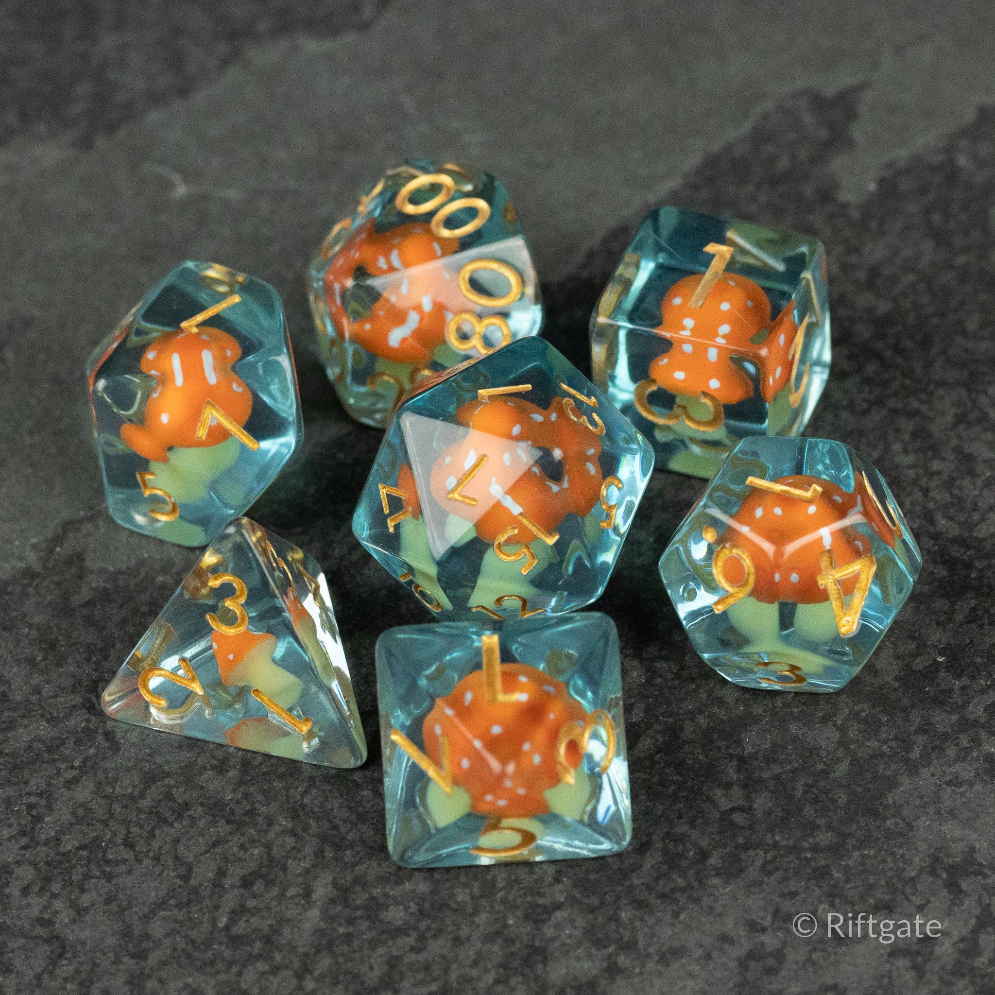 Orange + Blue Resin Mushroom Dice Set - Set of seven transparent resin dice with orange mushroom inclusions and gold numbers on dark surface.