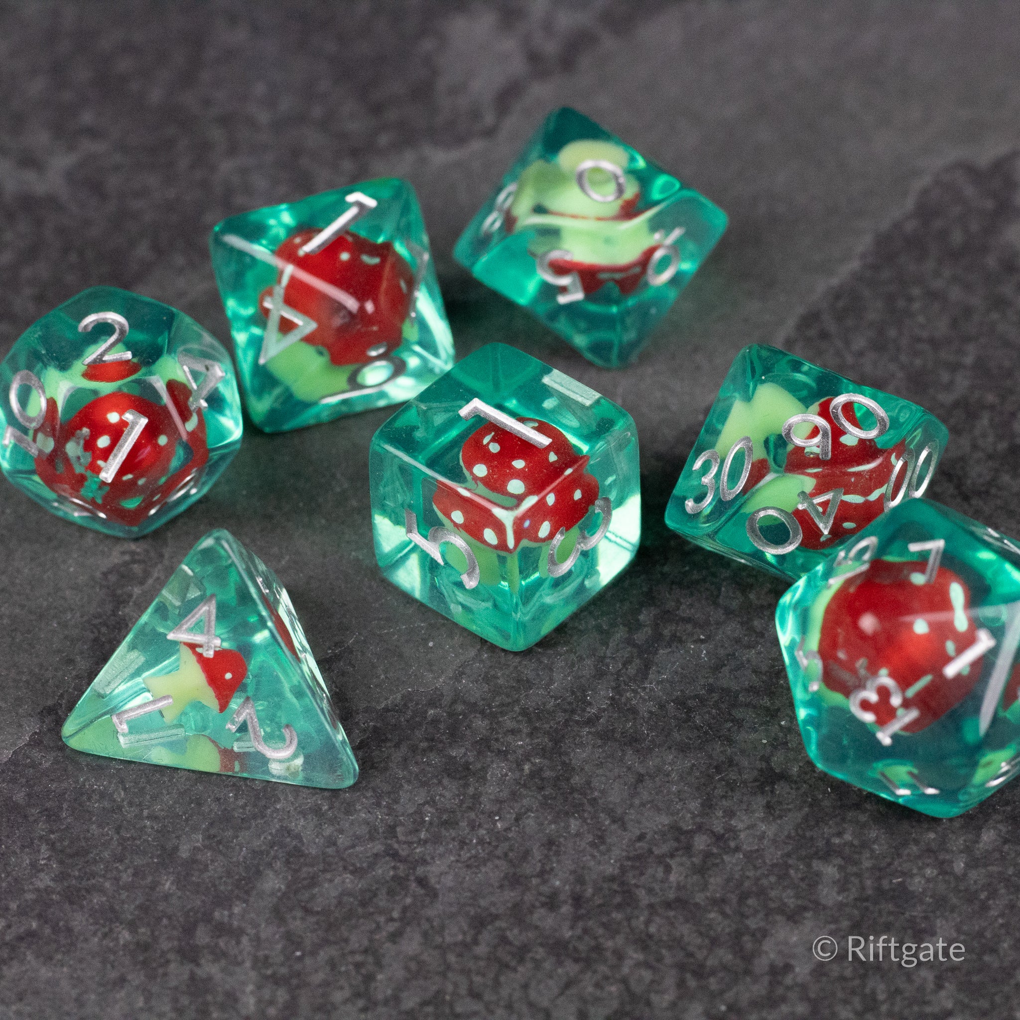 Red + Green Resin Mushroom Dice Set - Transparent green resin dice with embedded red mushrooms and white numbering on a dark surface.