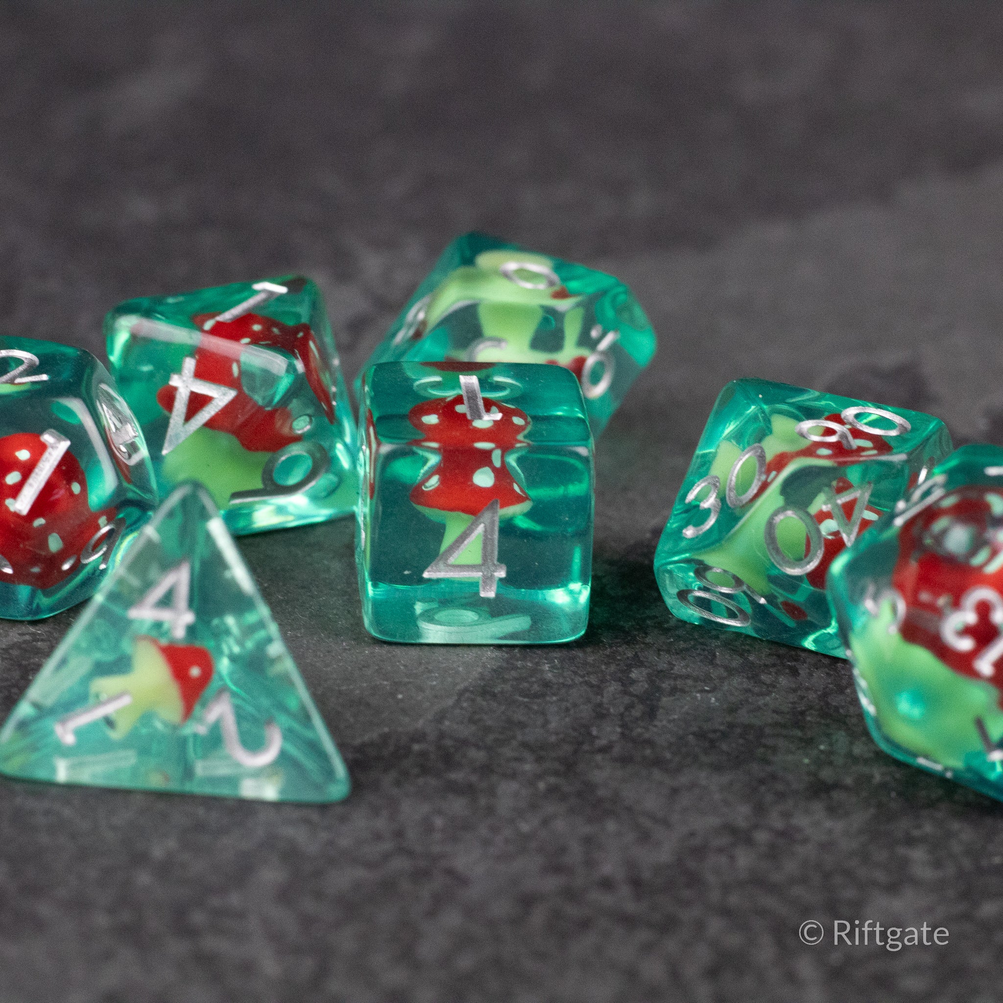 Red + Green Resin Mushroom Dice Set - Translucent green resin dice set with red mushroom inclusions and white numbering on gray surface.
