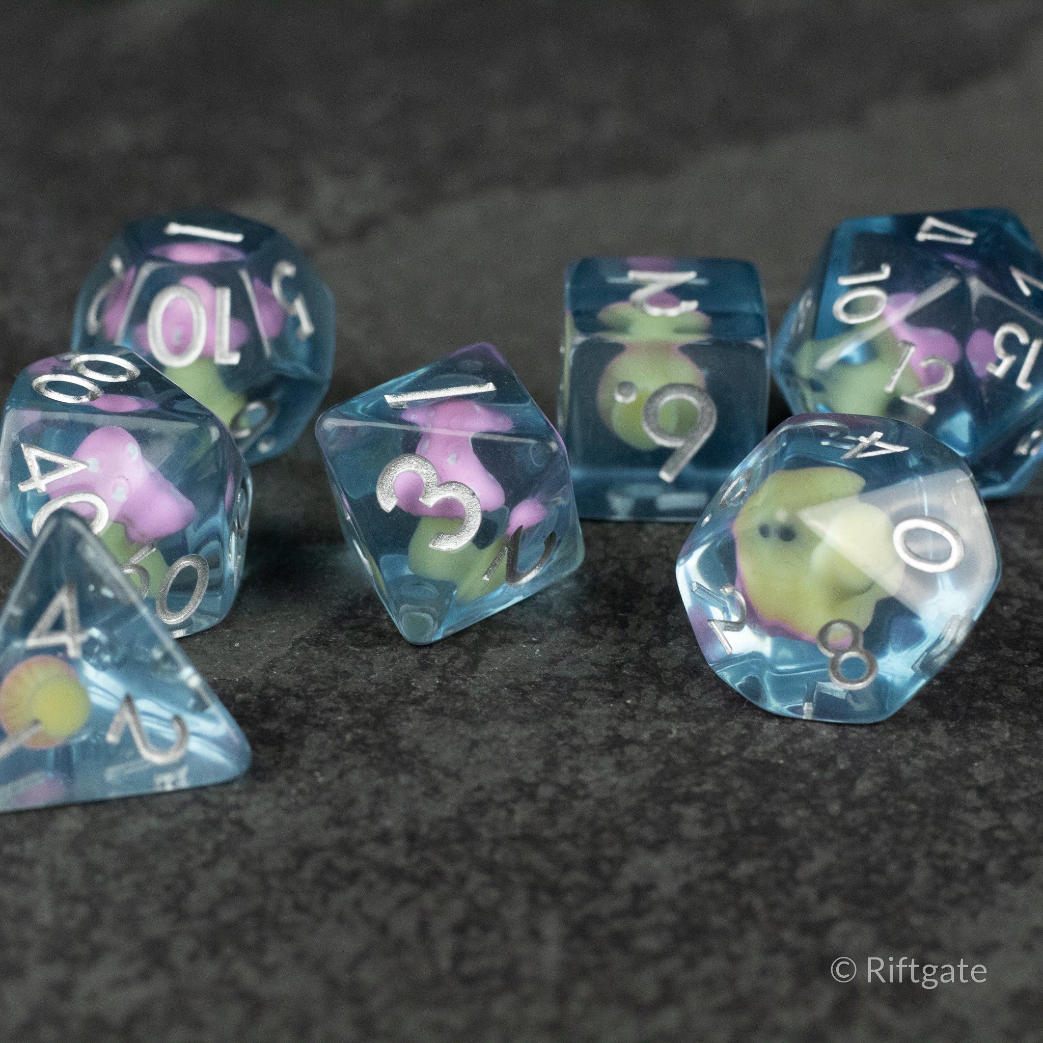 Pink + Blue Resin Mushroom Dice Set - Transparent blue resin dice with pink and cream mushroom inclusions, white numbering, various polyhedral shapes.