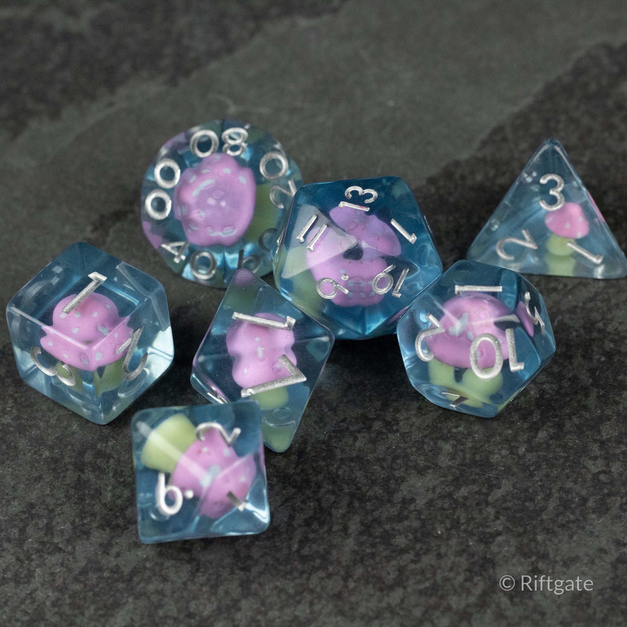 Pink + Blue Resin Mushroom Dice Set - Blue resin dice set with pink mushroom inclusions, featuring various polygon shapes and white numbering.