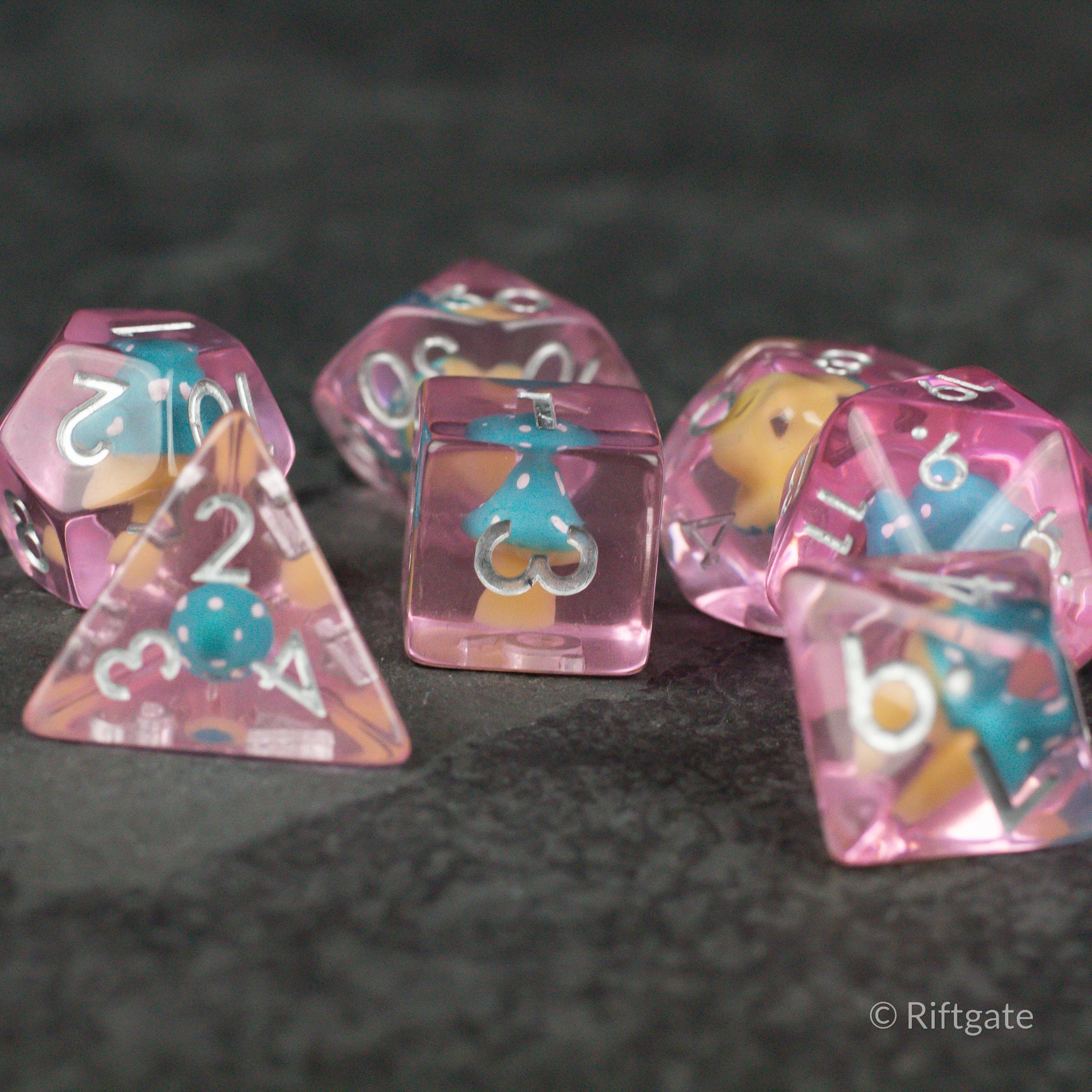Blue + Pink Resin Mushroom Dice Set - Translucent pink resin dice with blue and white mushroom inclusions, featuring various polygon shapes and gold numbers.