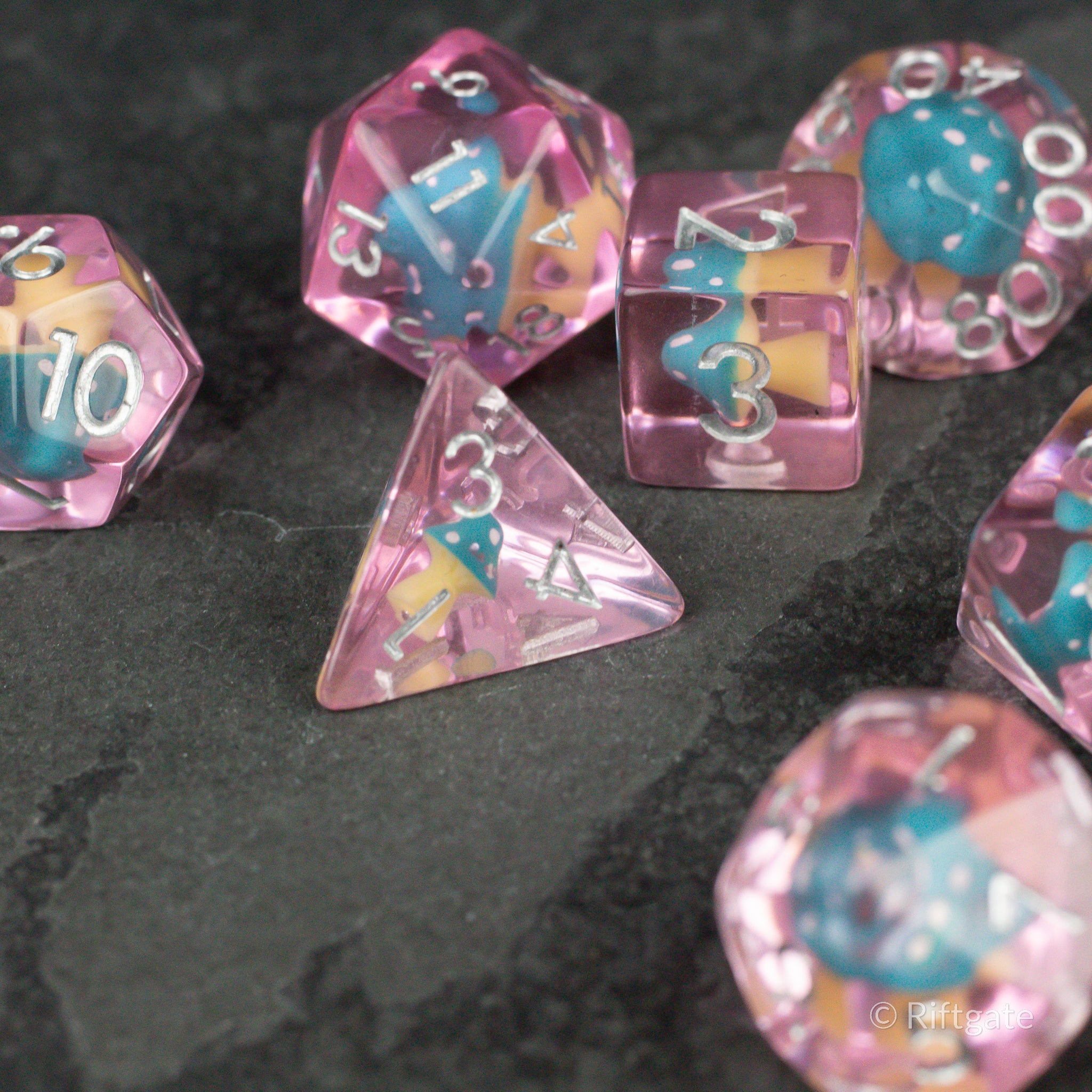 Blue + Pink Resin Mushroom Dice Set - Set of translucent pink resin dice with blue mushroom inclusions and white numbering on black surface.