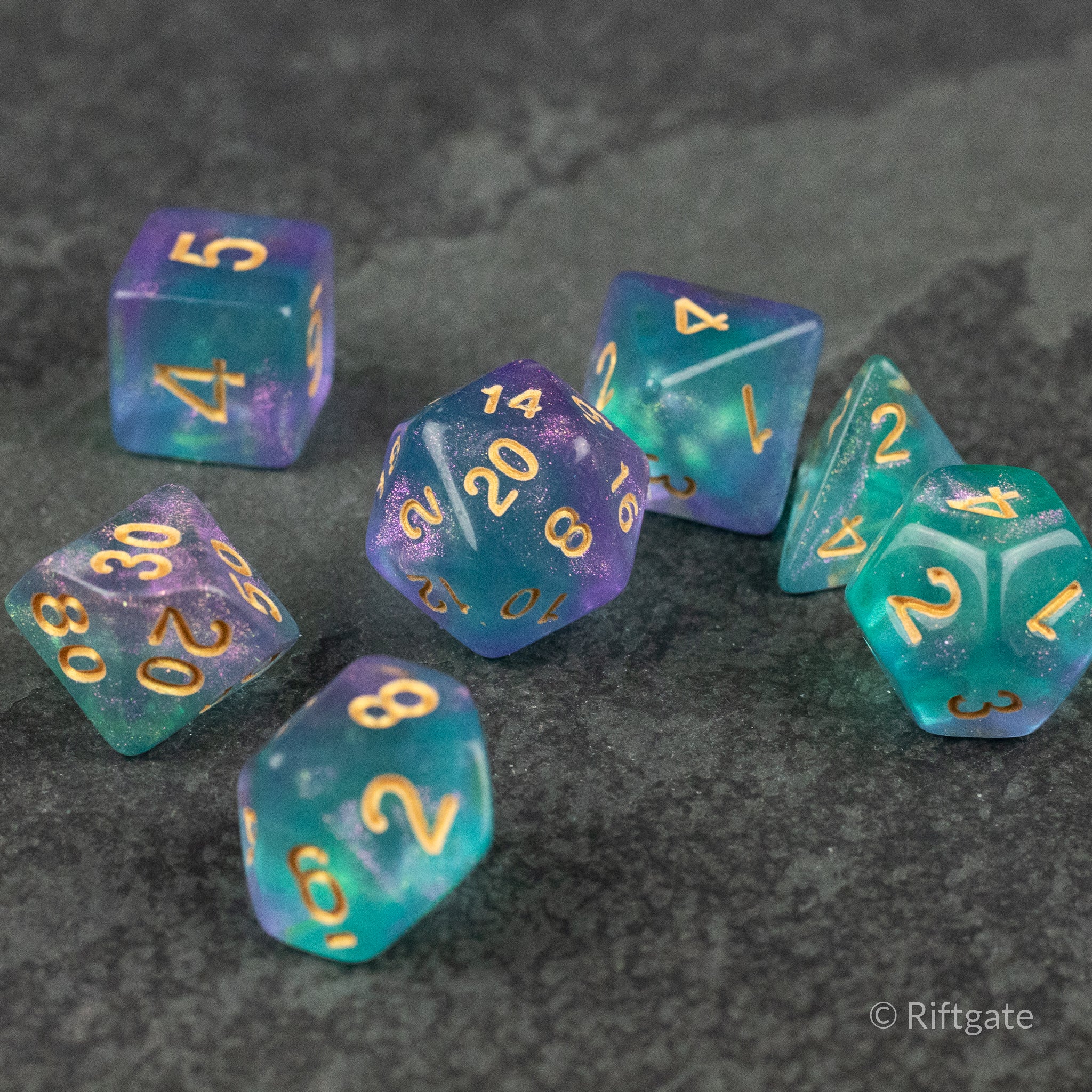 Faerie Glitter Dice Set - Set of seven polyhedral dice in translucent blue and purple with gold numbers and shimmering glitter accents.