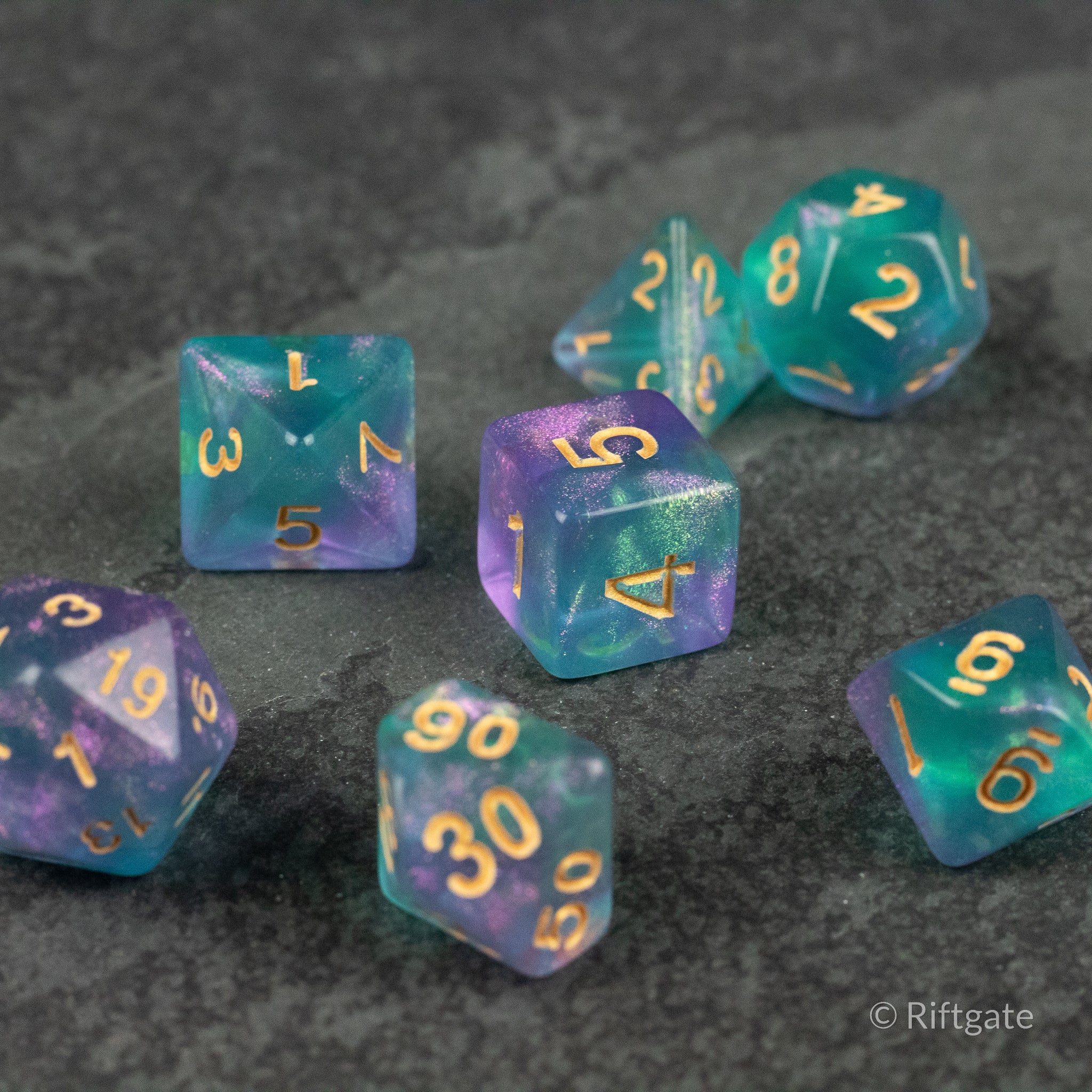 Faerie Glitter Dice Set - Seven translucent polyhedral dice in swirling blue and purple hues with gold numbering, designed for tabletop gaming.