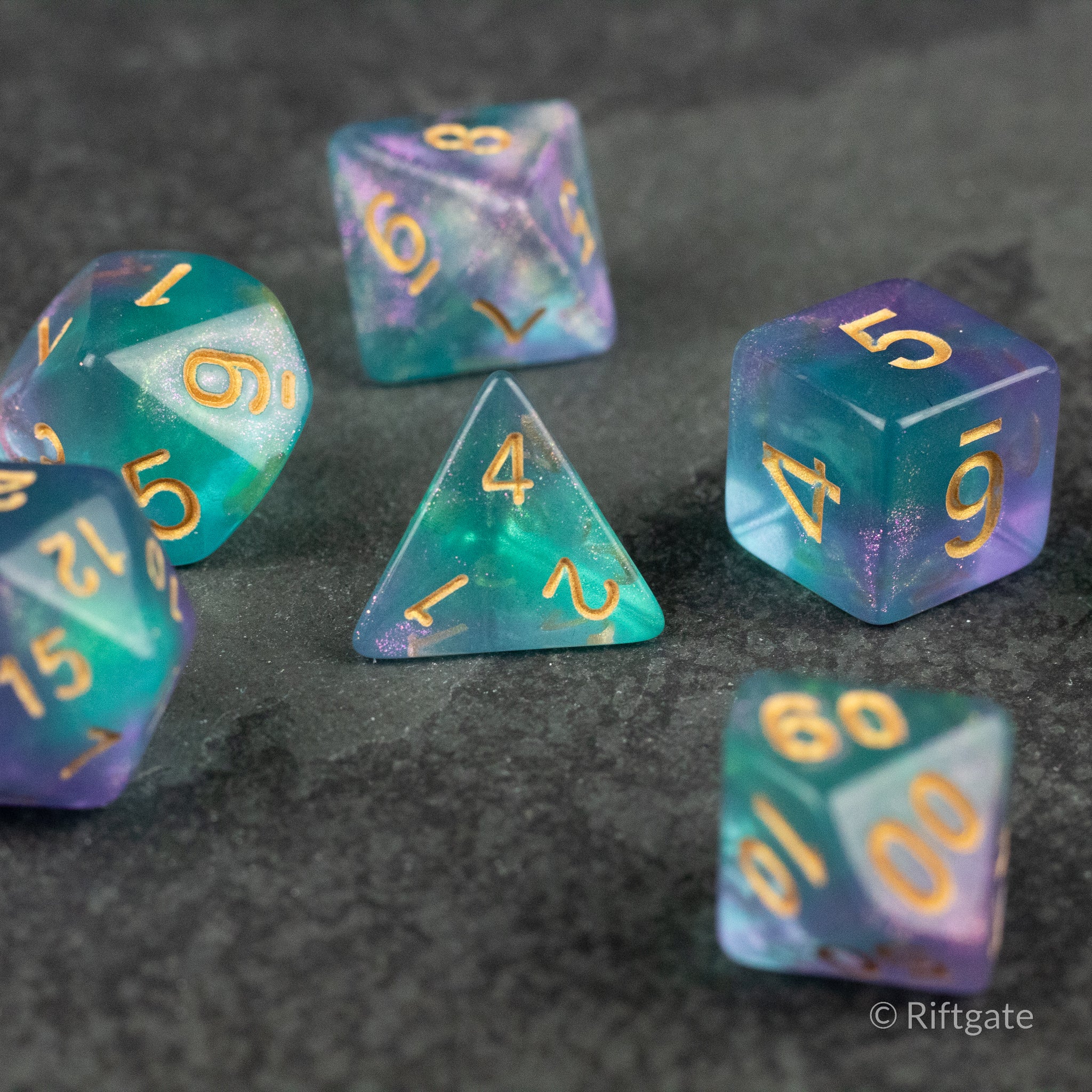 Faerie Glitter Dice Set - Set of translucent purple and teal polyhedral dice with gold numbers, featuring a glittery, faerie-inspired design.