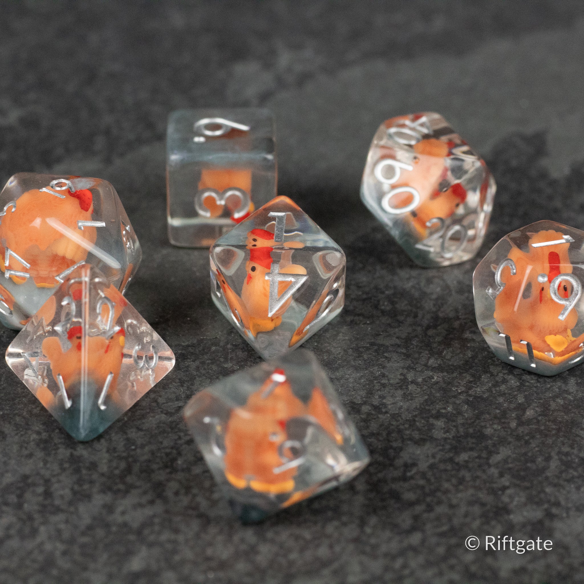 Chicken Dice Set - Set of transparent polyhedral dice with embedded miniature orange chicken figurines and white numbering on a dark textured.
