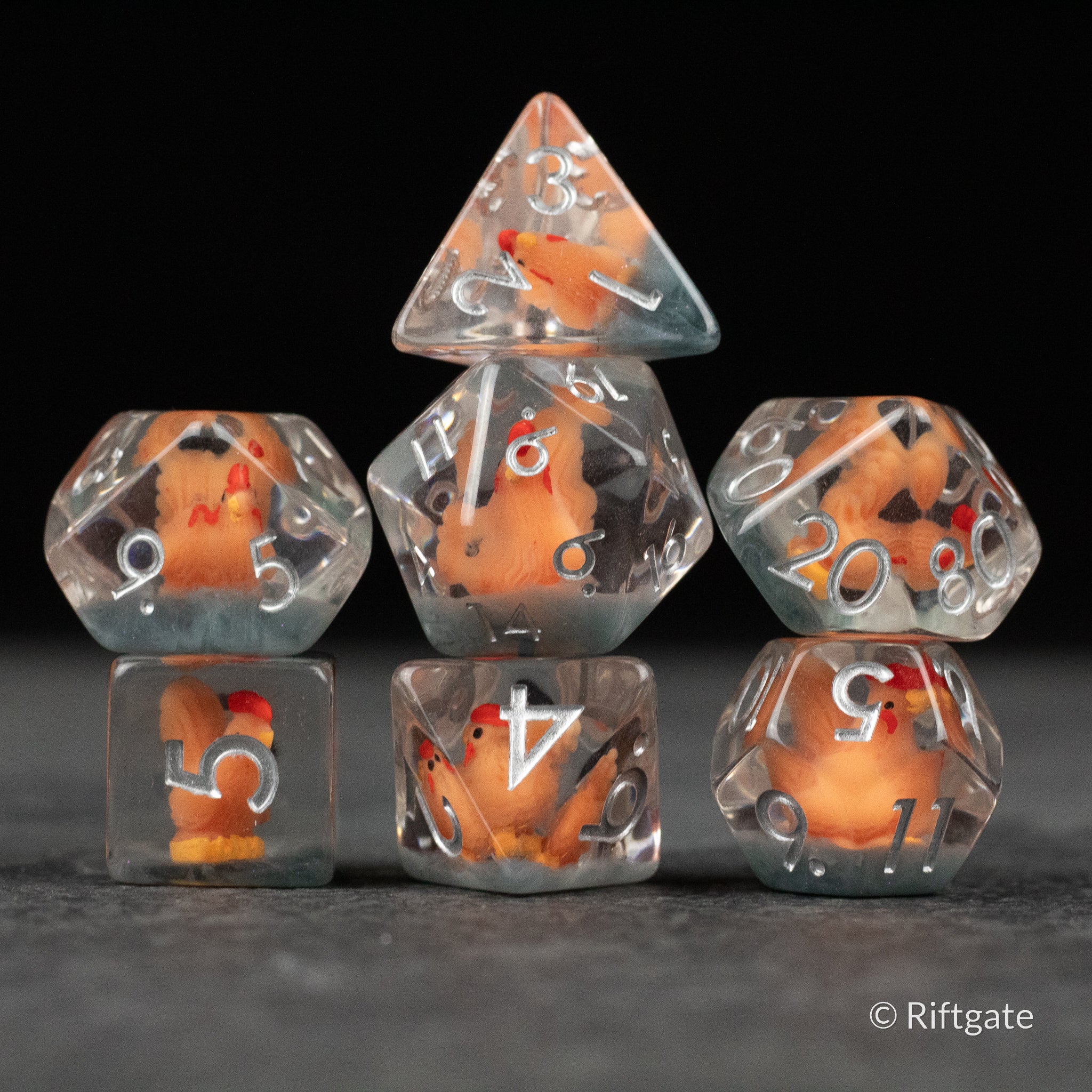 Chicken Dice Set - Set of seven clear polyhedral dice with embedded small orange and white chicken figures, featuring white numbers.