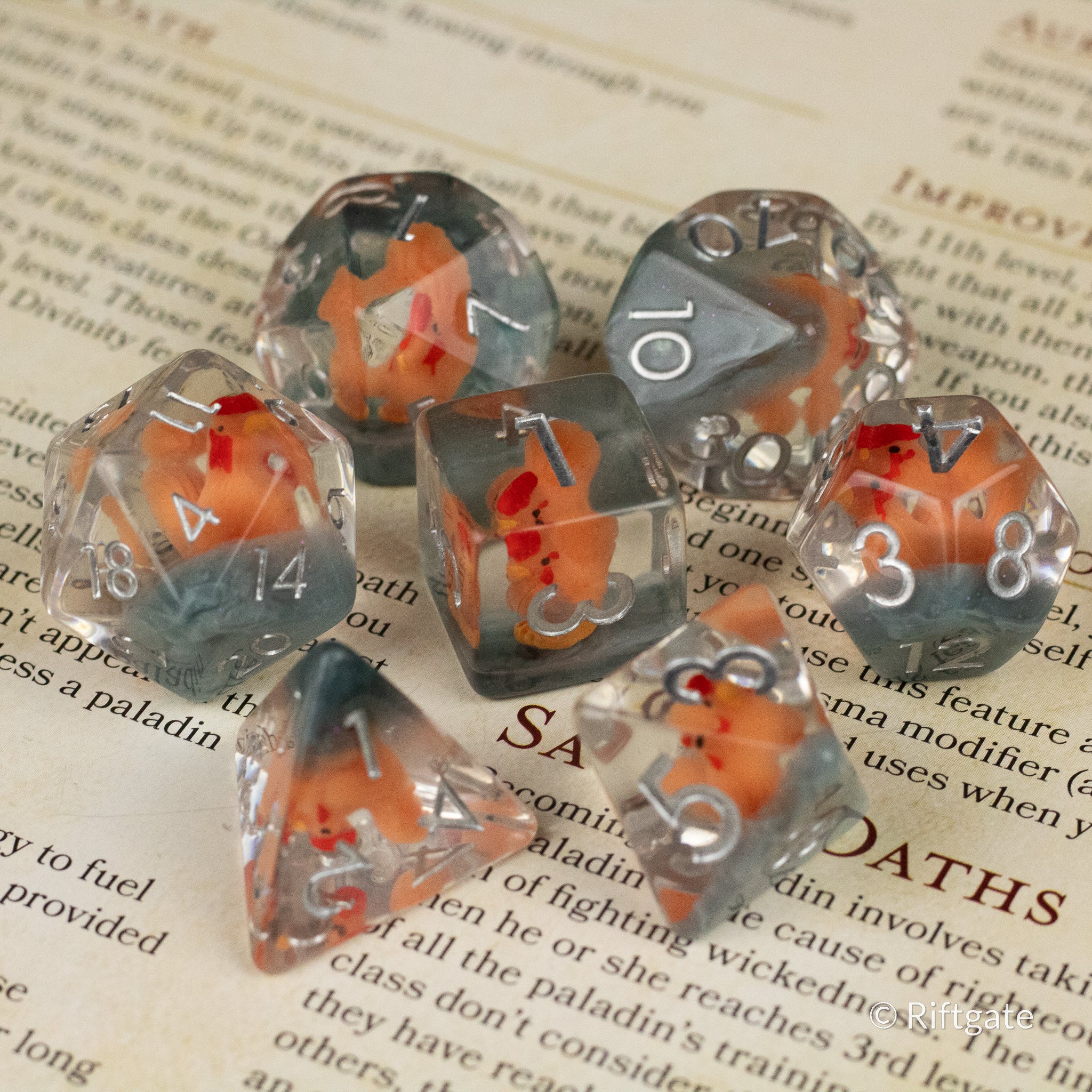 Chicken Dice Set - Set of seven transparent polyhedral dice with orange chicken illustrations inside and white numbers on each face.