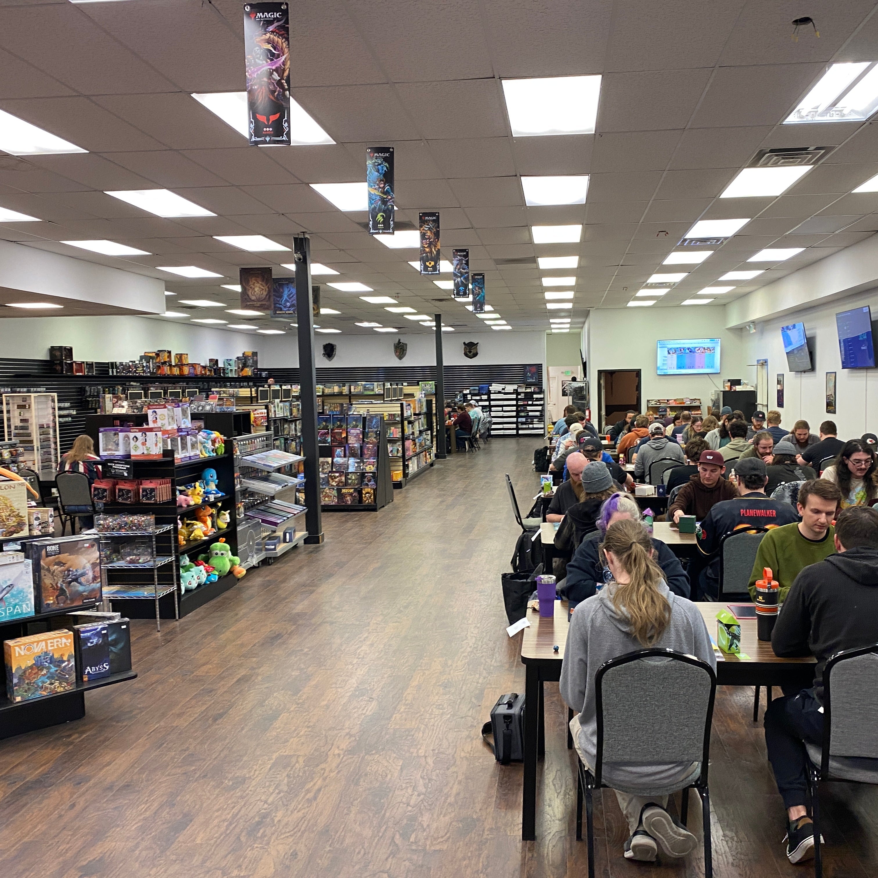 People sitting at tables in a large store with shelves and a TV on the wall.