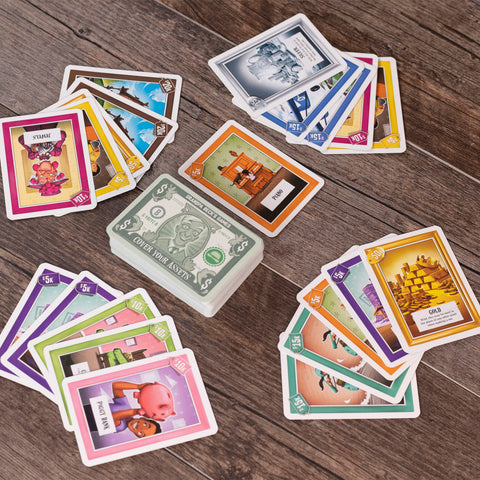 Cover Your Assets - Cover Your Assets card game with colorful character and asset cards fanned around a central money deck on a wooden table.
