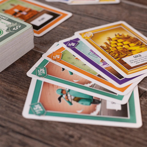 Cover Your Assets - Colorful rectangular playing cards from the Cover Your Assets game, featuring illustrations and icons, spread out on a.