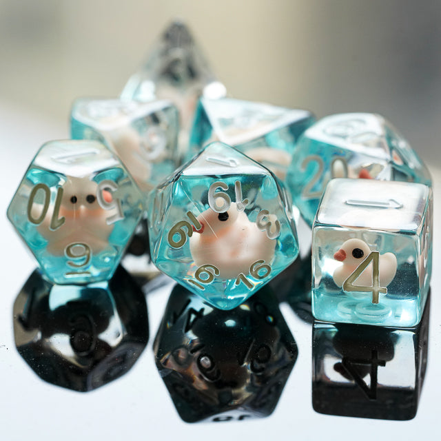 White Duck Dice Set - Transparent dice with white duck figurines inside and gold numbering, set of seven on reflective surface.