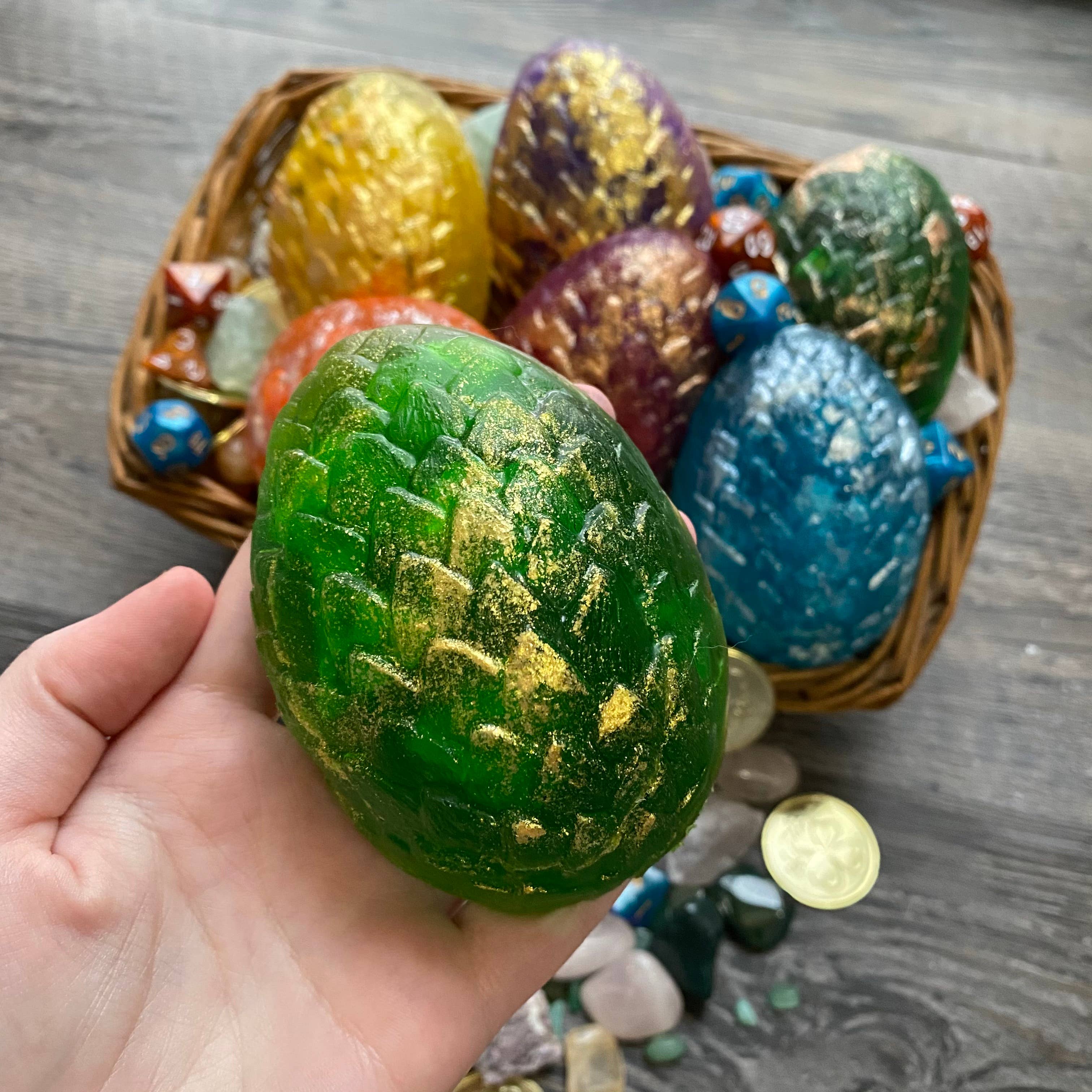Dragon Egg Dice Soap - Green dragon egg soap with gold scale detailing held in hand, more colorful dragon egg soaps in woven basket in background.