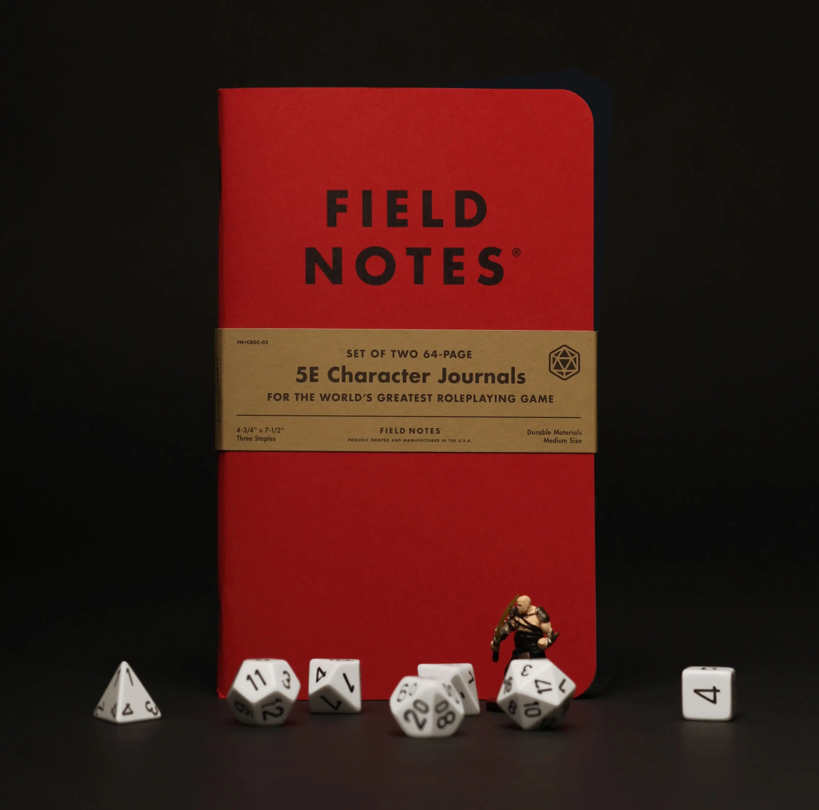 5E Character Journals - Red 5E Character Journal with tan wraparound label, surrounded by white polyhedral dice and a miniature figure.