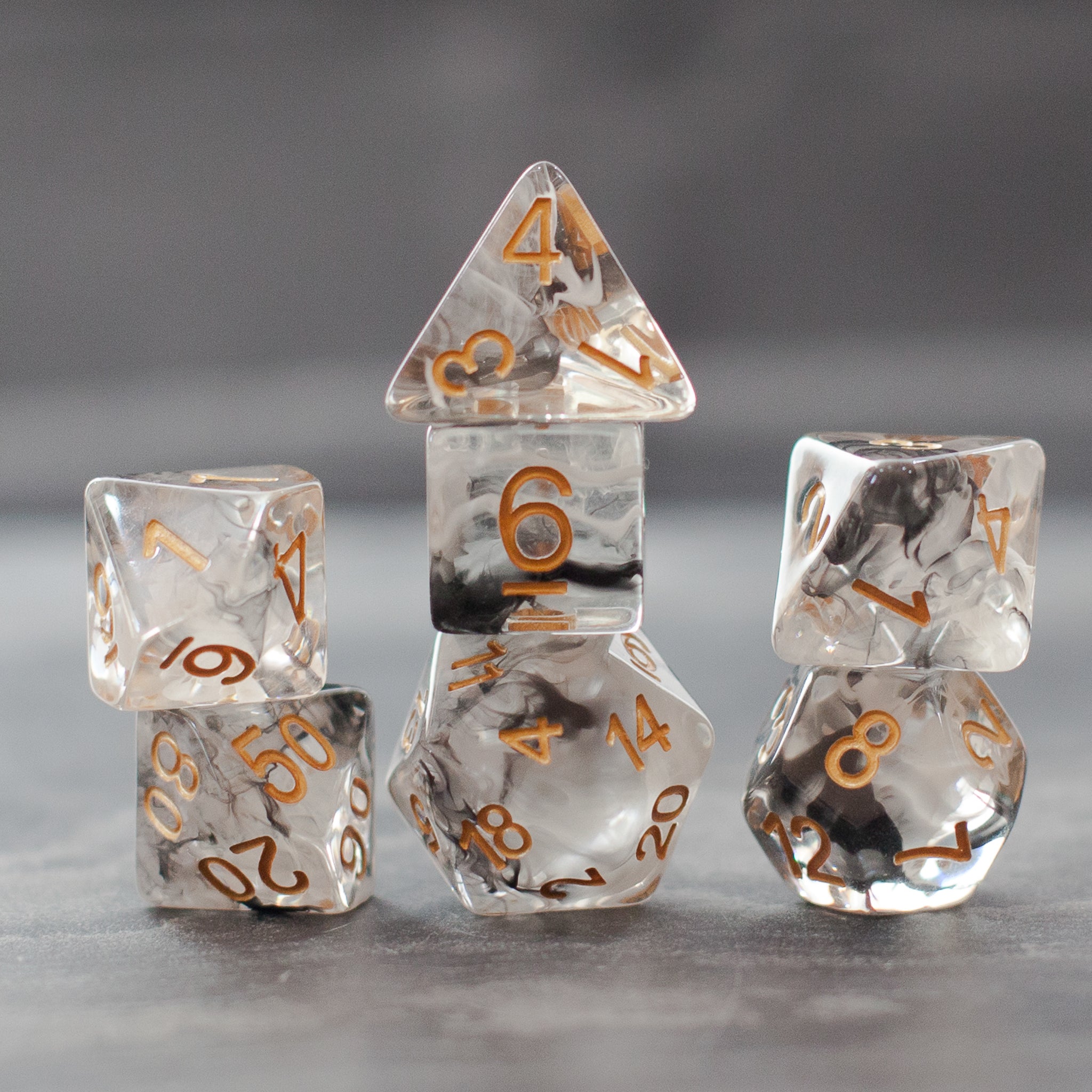 Black & White Smoke Dice Set - Set of clear dice with black smoke swirls and gold numbers, including d4, d6, d8, d10, d12, and d20 shapes.