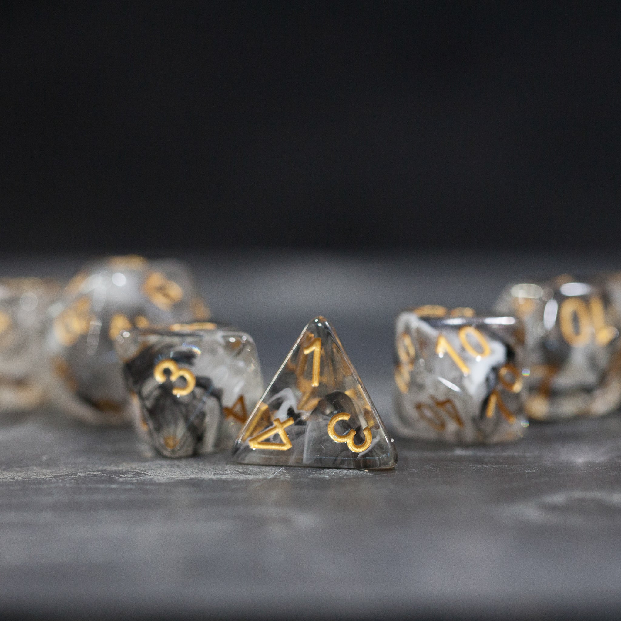 Black & White Smoke Dice Set - Black and white smoke effect dice with gold numbers, including a four-sided die in focus on a dark surface.