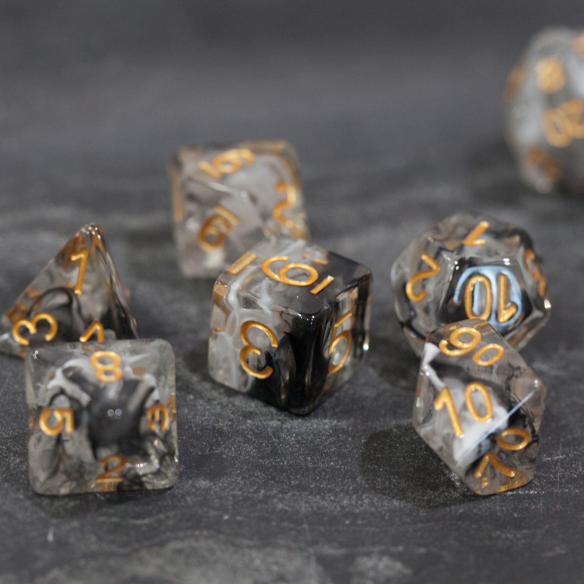 Black & White Smoke Dice Set - Set of translucent black and white smoke effect polyhedral dice with gold numbering on a dark surface.