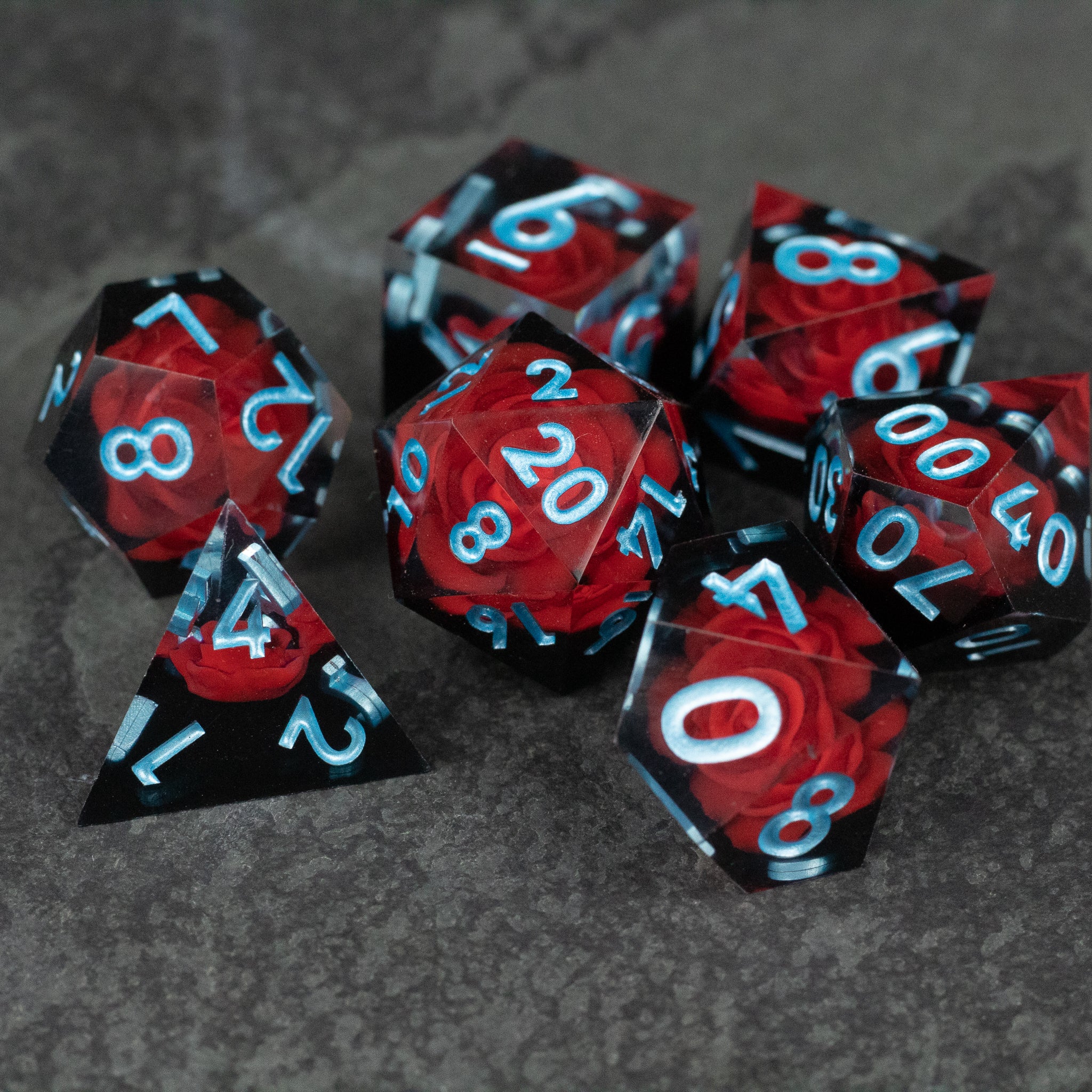 Cursed Rose Dice Set - Set of seven sharp-edged dice with deep red and black marbled pattern and sky blue numbers.