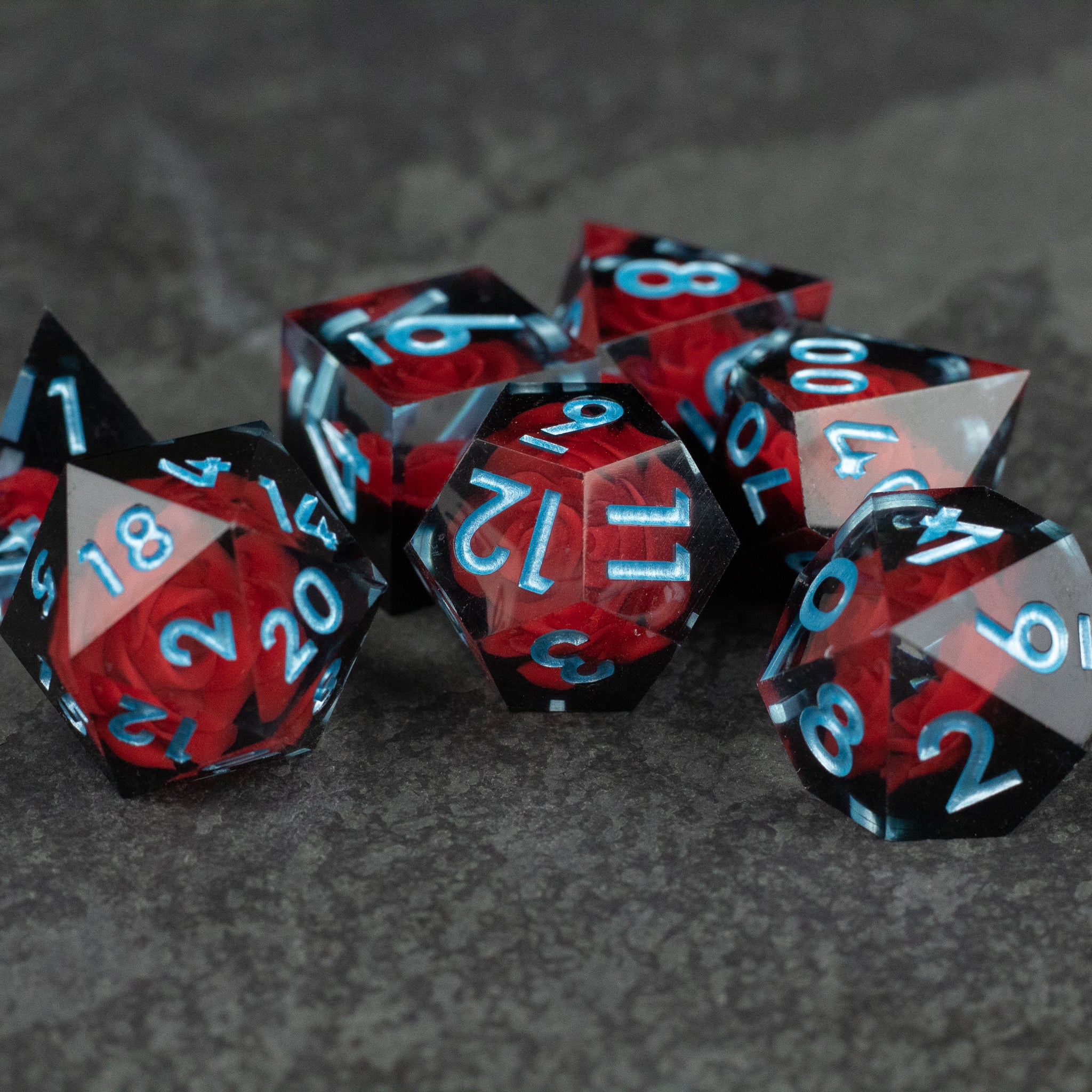 Cursed Rose Dice Set - Set of seven sharp-edged dice with black, red, and translucent blue color patterns and white numbers.