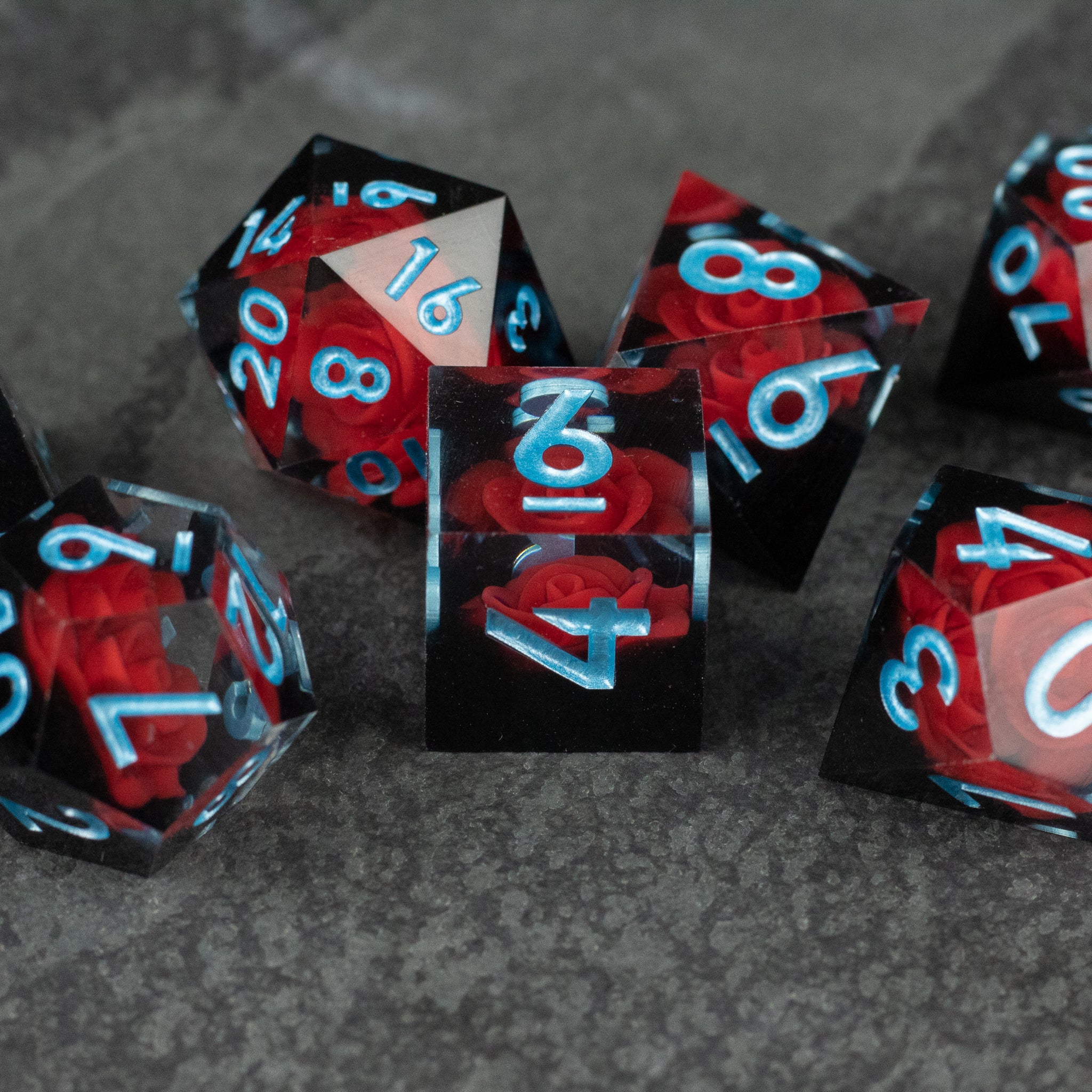 Cursed Rose Dice Set - Set of seven sharp-edged dice with swirling black and deep red marbled patterns and bright blue numbers.